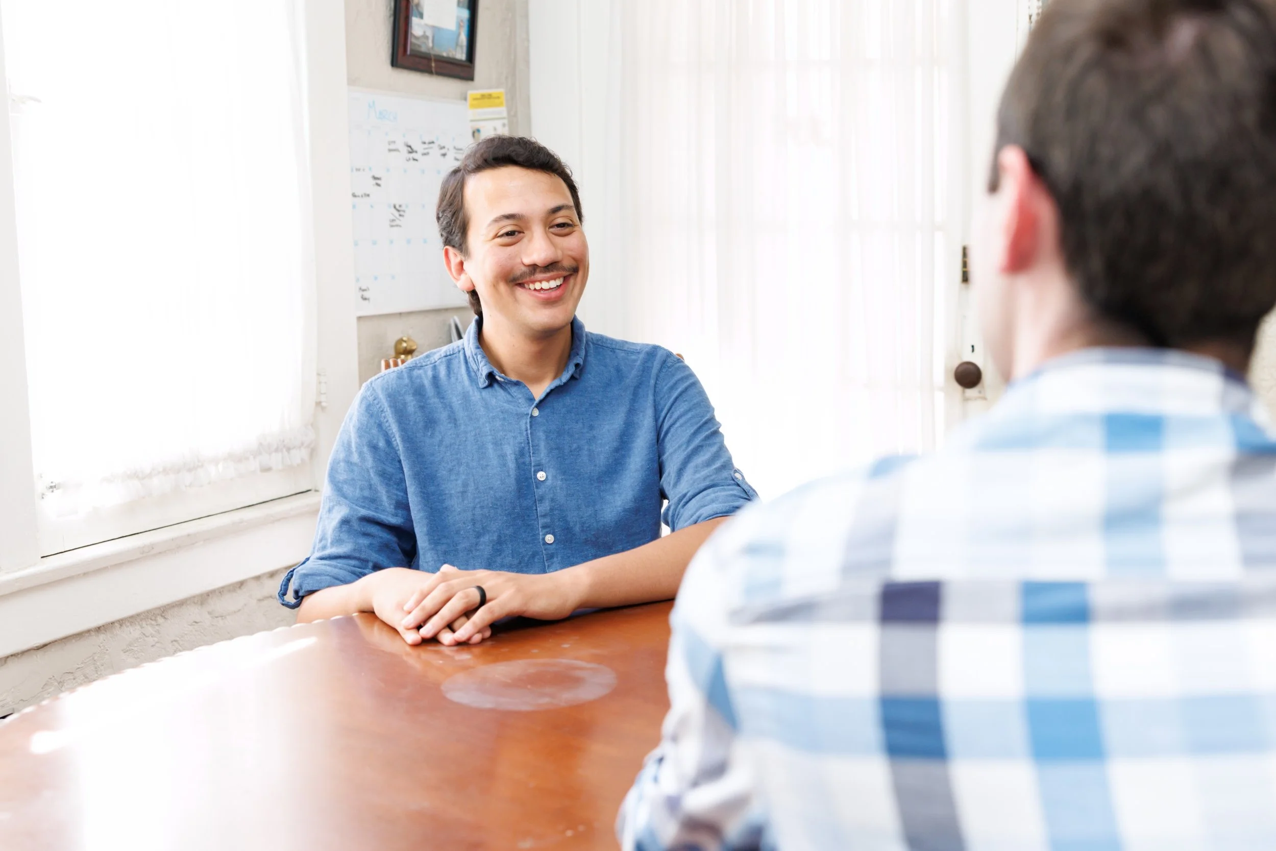 Two men having a conversation in office with whiteboard and window in background.