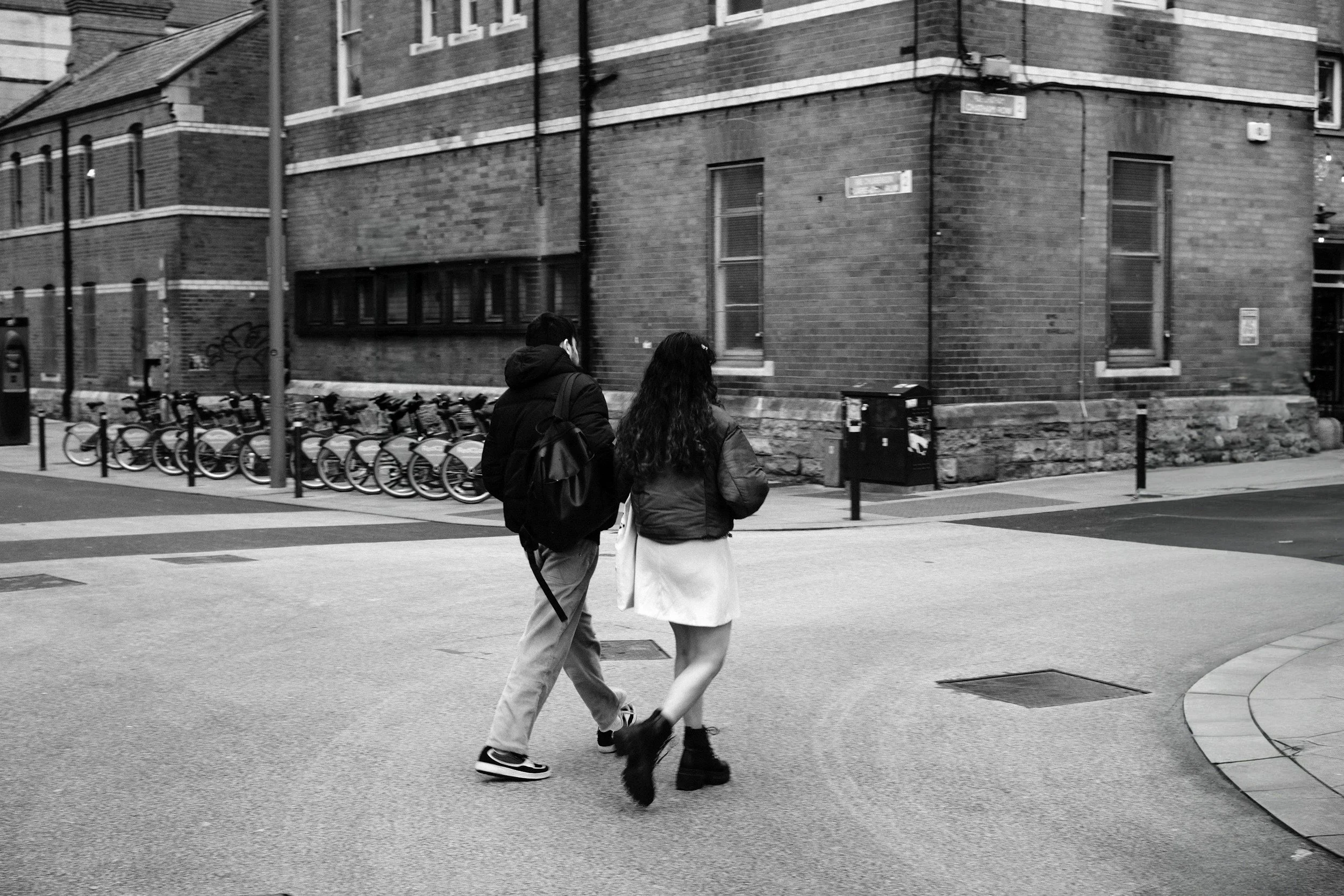 Black and white photo of a couple walking across a city street, representing everyday connection and relationship dynamics.