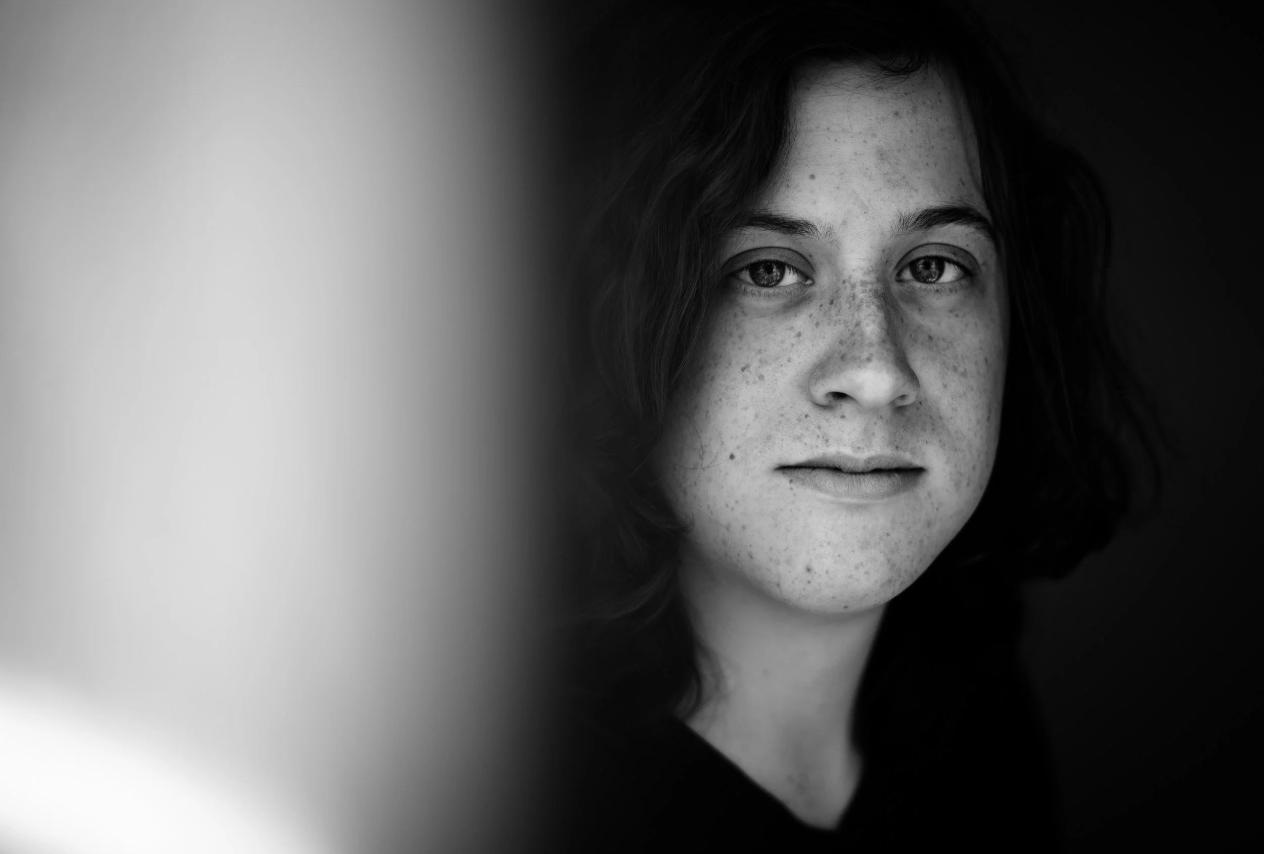 Black and white close-up portrait of a freckled woman looking directly at the camera, conveying reflection, depth, and emotional presence.