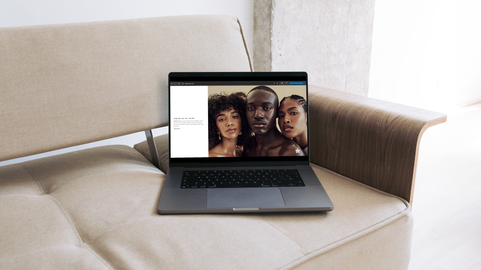 A laptop on a light-colored couch displaying a brand studio portfolio with an open website that has a white left panel and right-side photo of three people with varied skin tones and features.