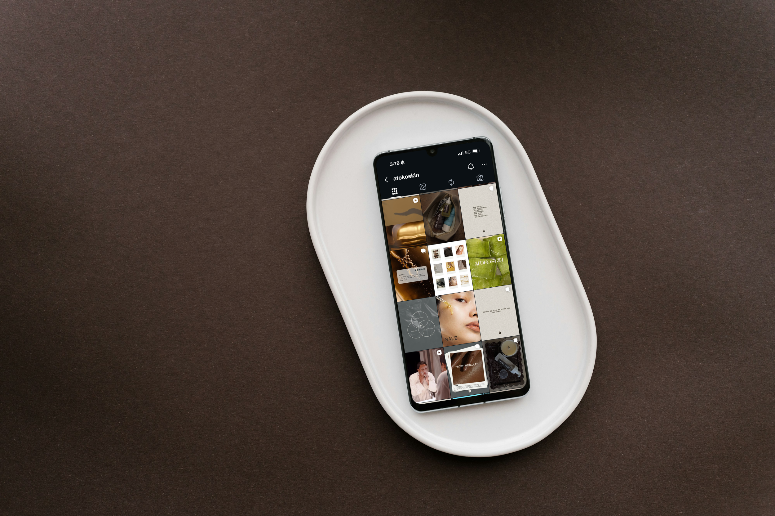Smartphone placed on a white tray shows an Instagram profile with images of beauty products and models, on a dark surface.