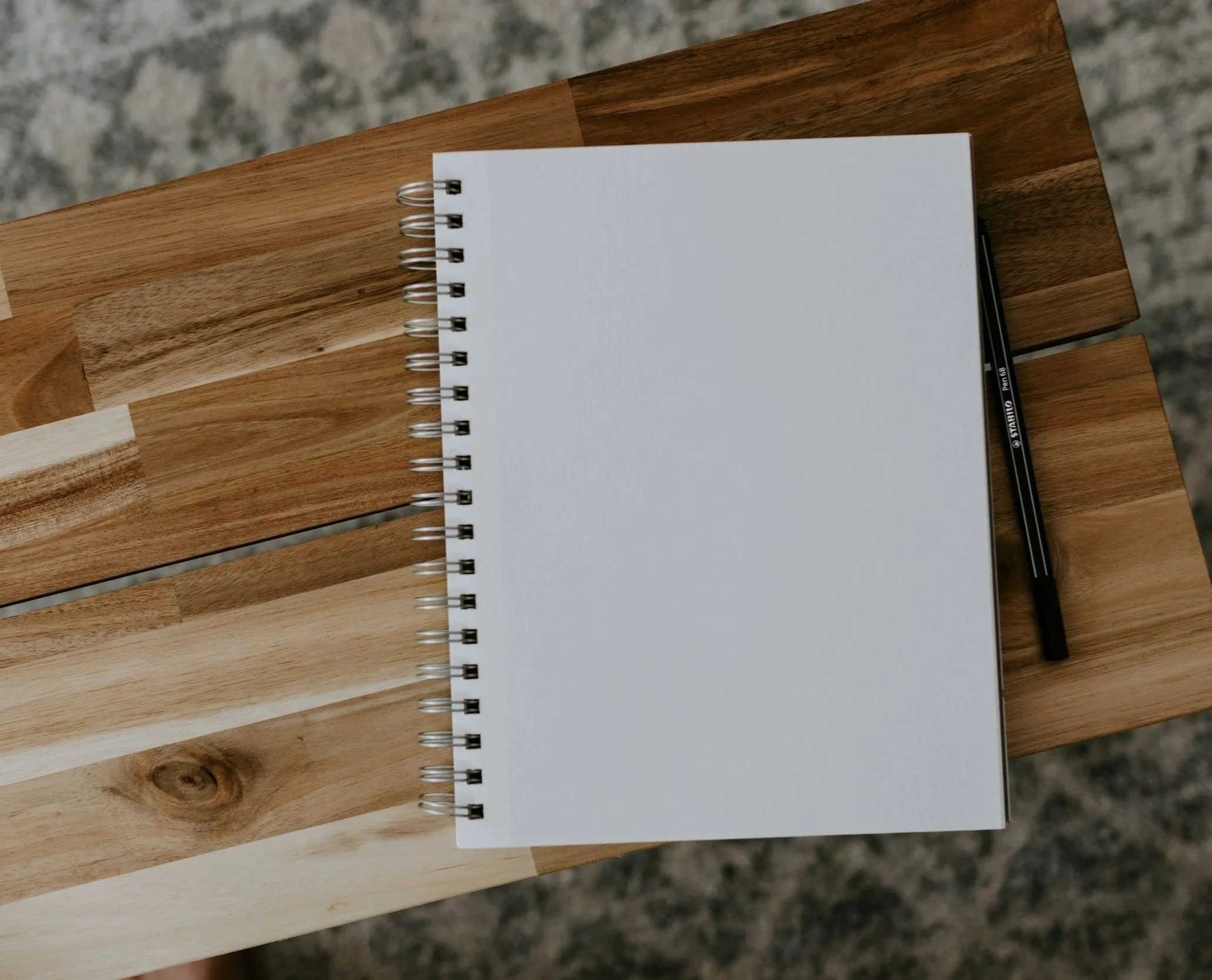 Empty spiral notebook with black pen resting on a wooden surface.