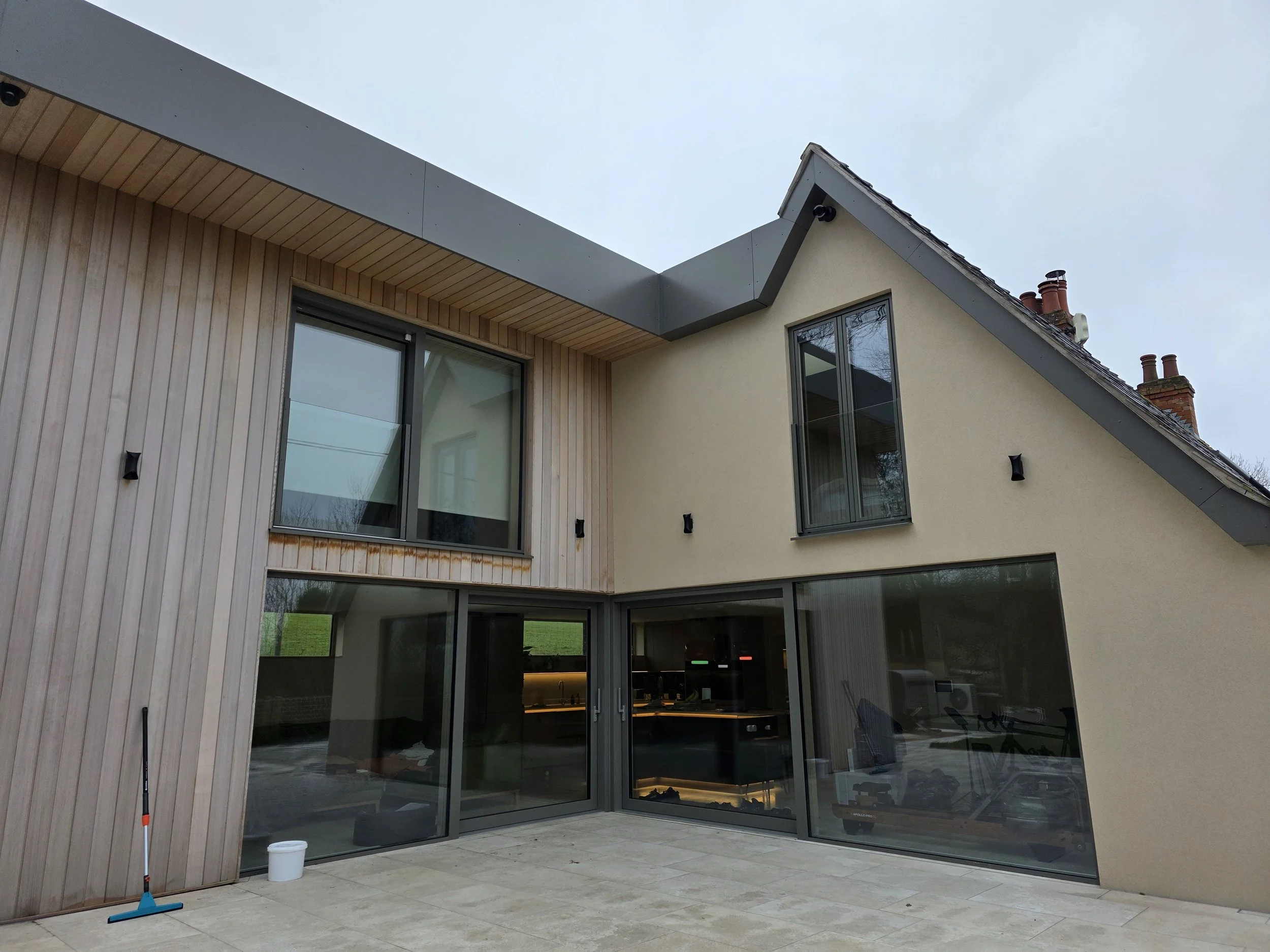 Modern house exterior with cream-colored and cedar-paneled walls, large glass doors and windows, a sloped roof, and outdoor patio area. all designed and built by cortis construction