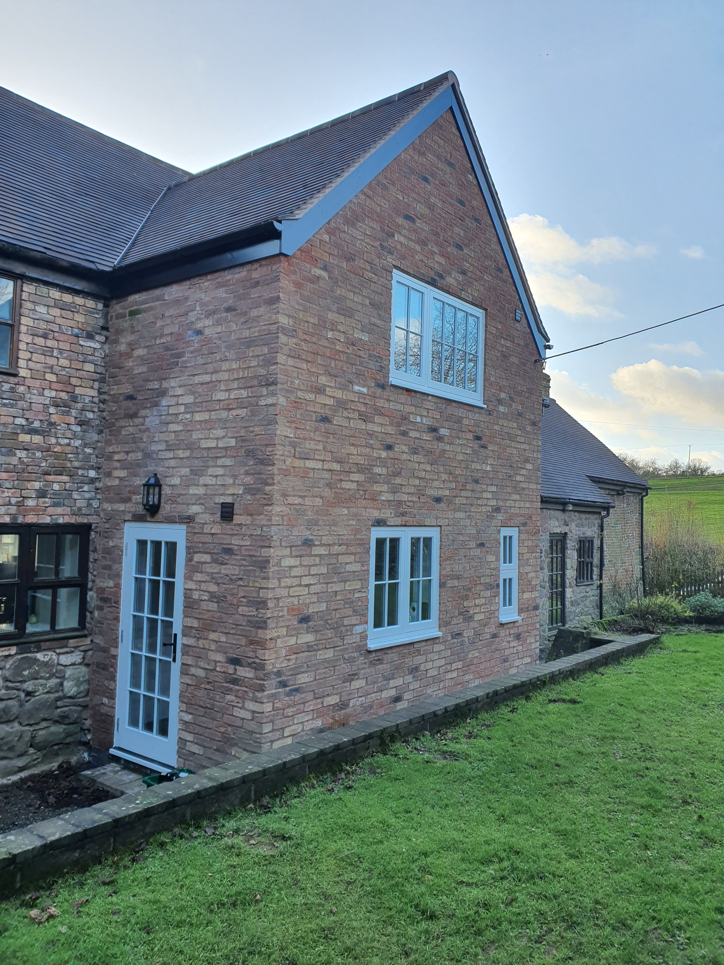 A brick house with white-framed windows and a glass-paneled door, situated on a grassy lawn under a partly cloudy sky. built by cortis construction in ludlow