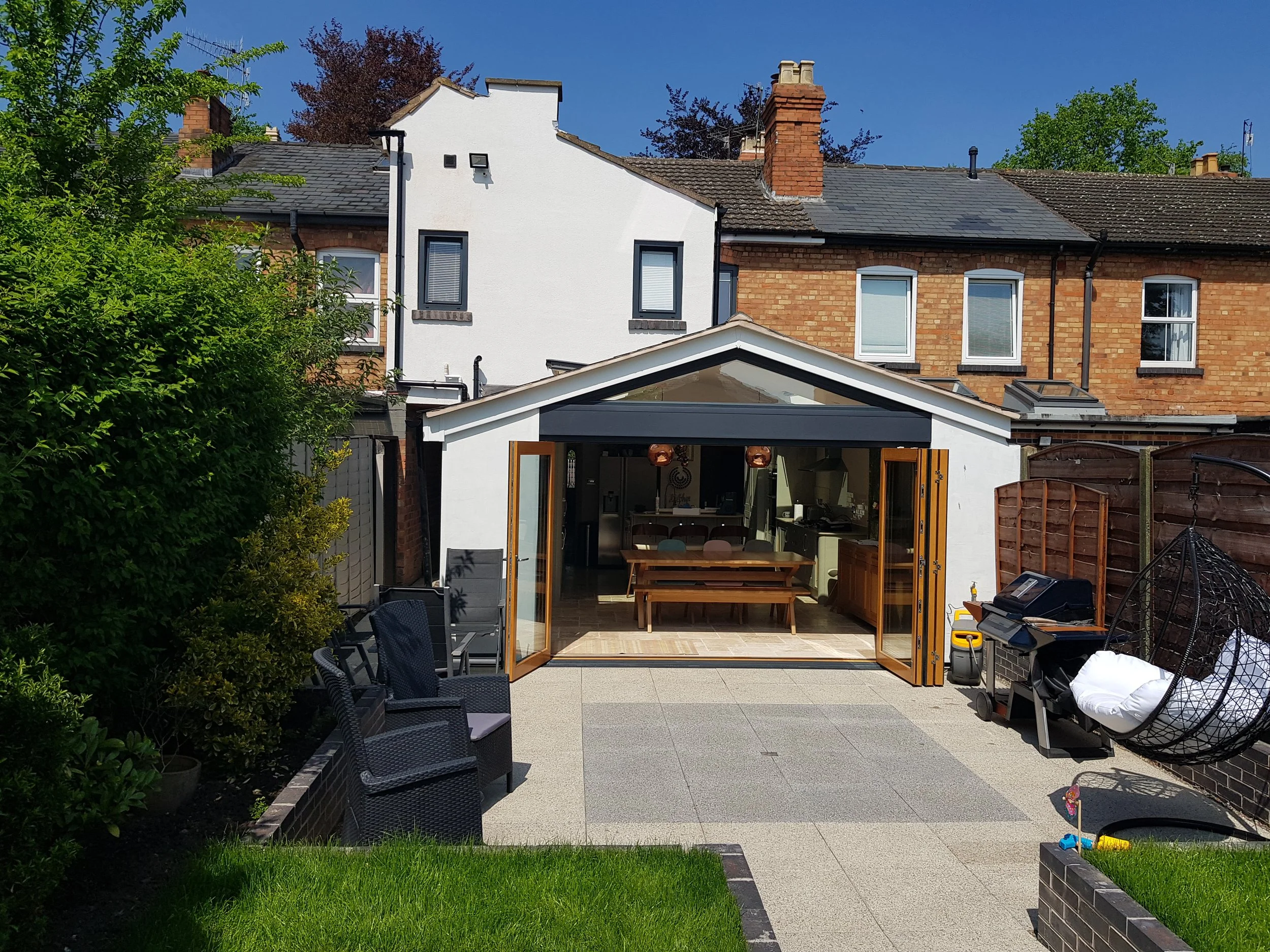 Backyard with outdoor seating, a modern garden room with open wooden doors, and a hanging egg chair on a sunny day.