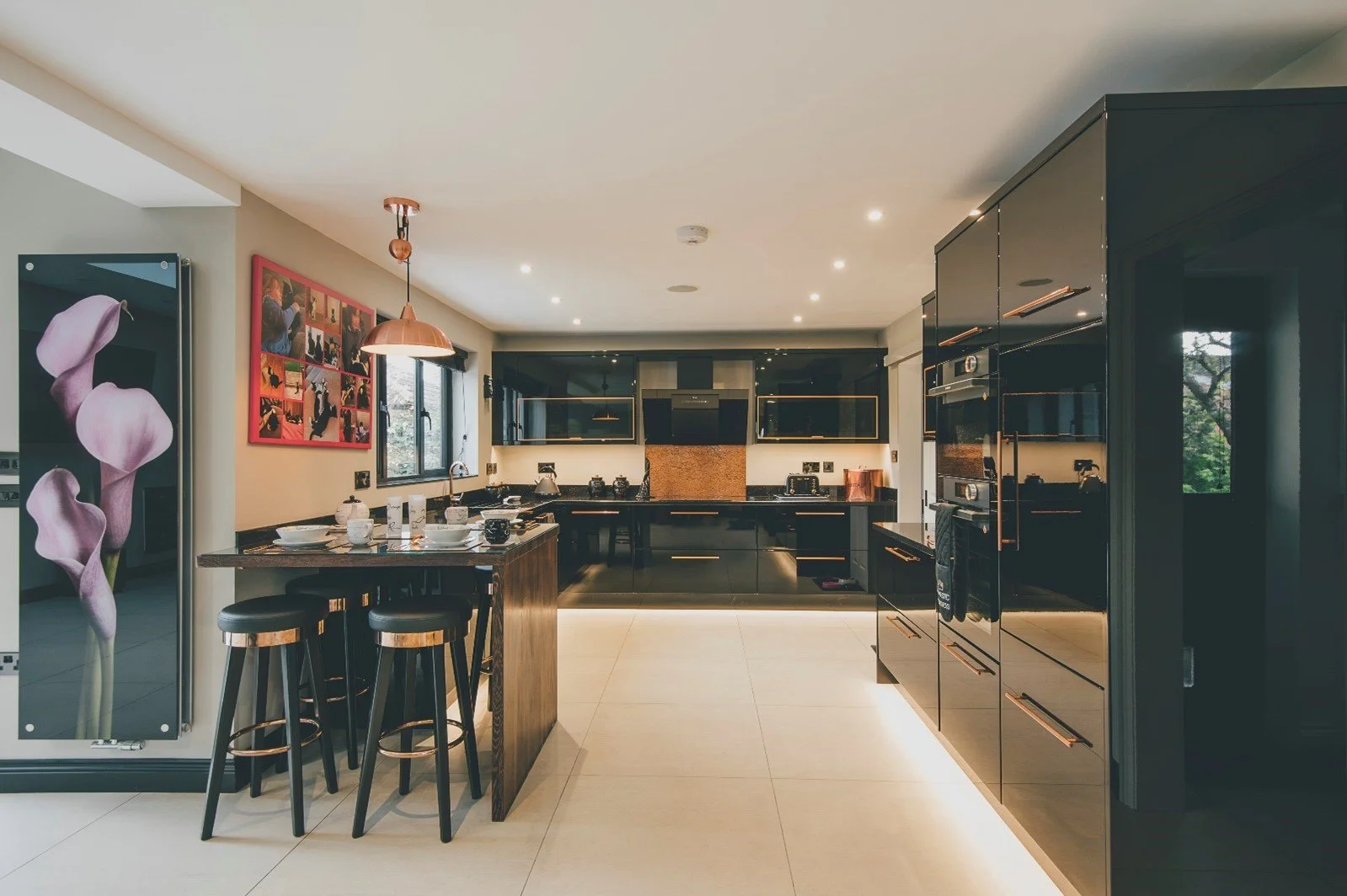 Modern black kitchen with glossy cabinets, built-in appliances, and a central island with bar stools, decorated with artwork and a pink pendant light. built by cortis construction
