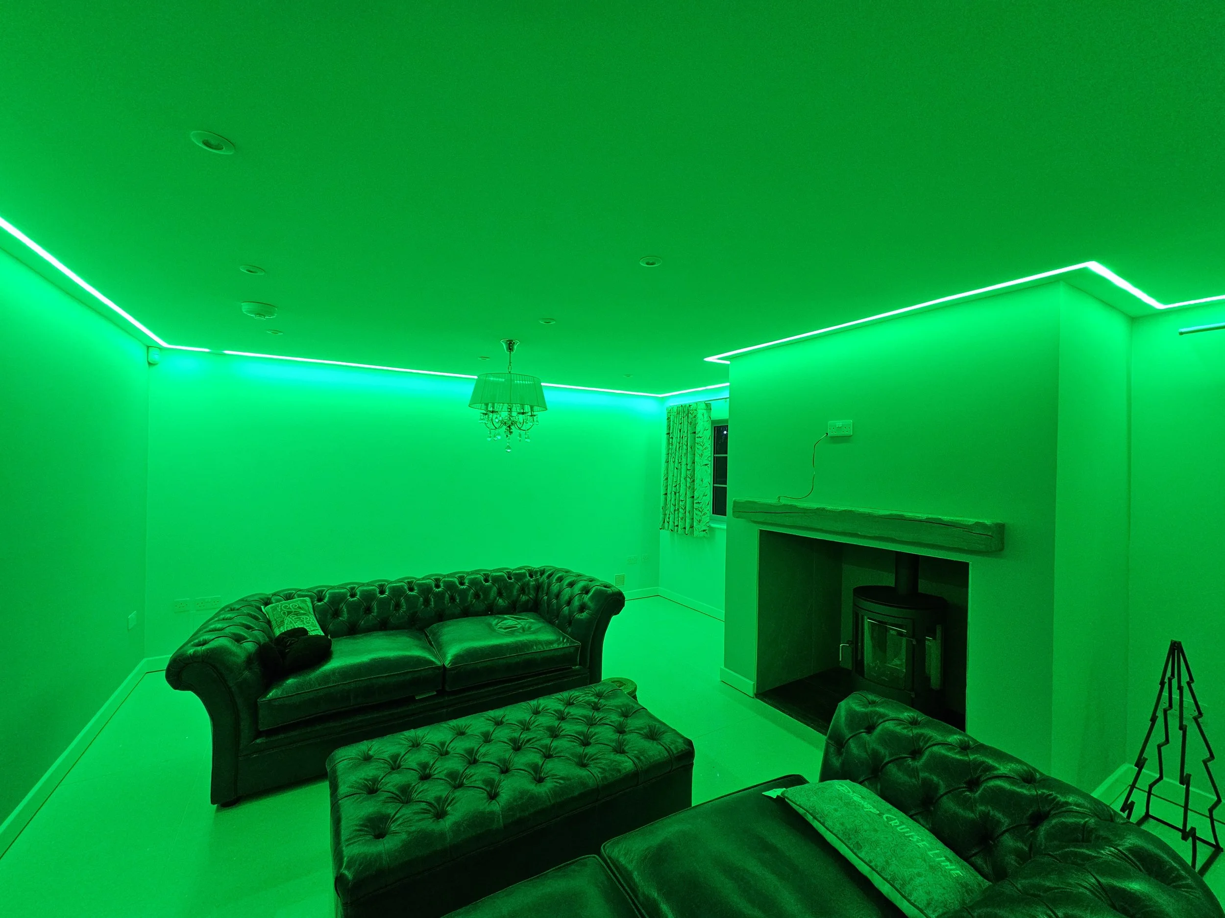 Living room illuminated with green LED lights, featuring leather sofas, a fireplace, and a chandelier.