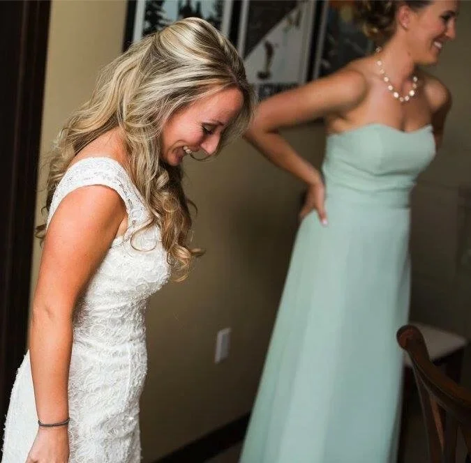 Two women in elegant dresses laughing and smiling indoors.