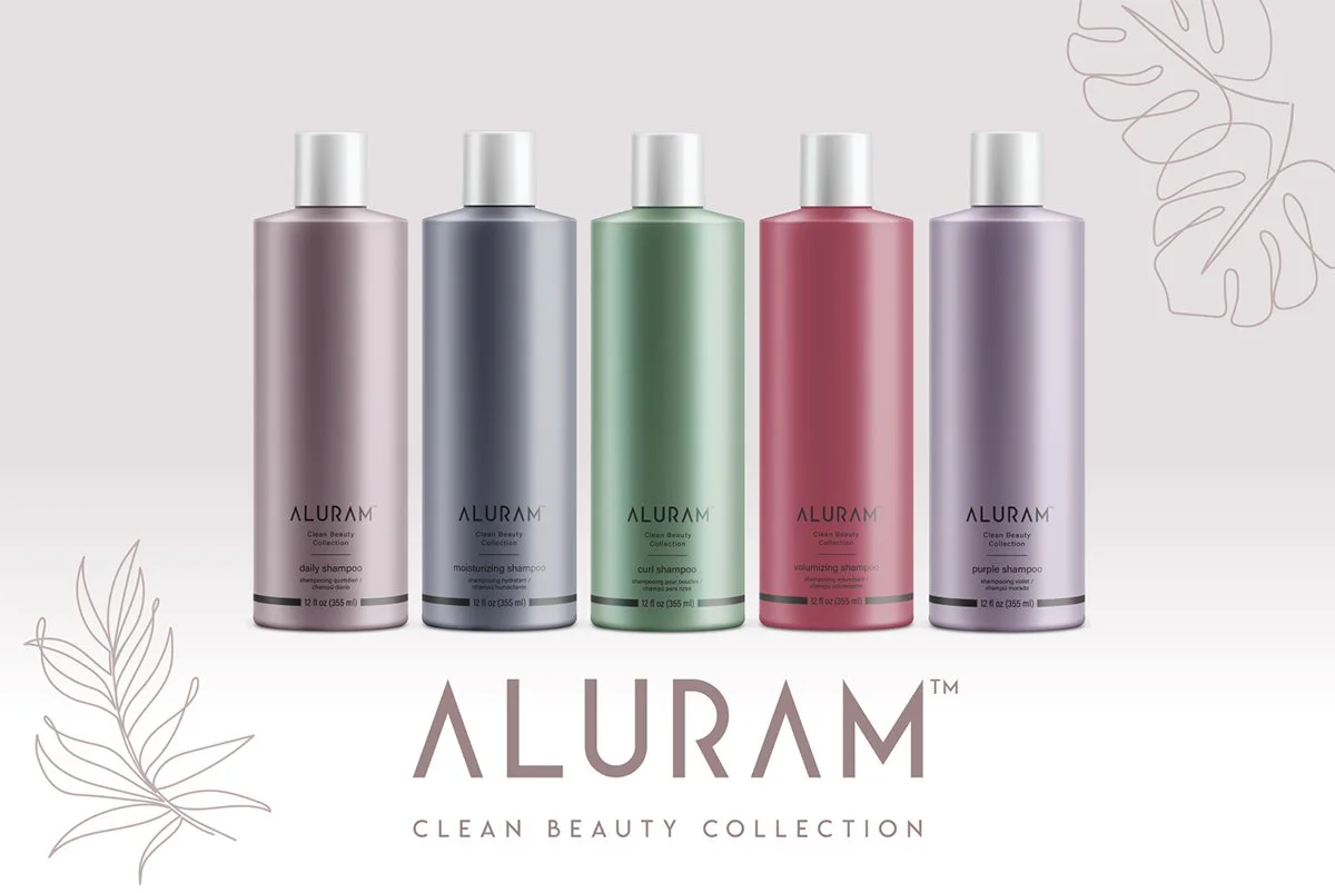 Five bottles of Aluram shampoo in different colors, arranged in a row with a plain background and leaf illustrations. The bottles are labeled for different types of shampoo in the Aluram Clean Beauty Collection.