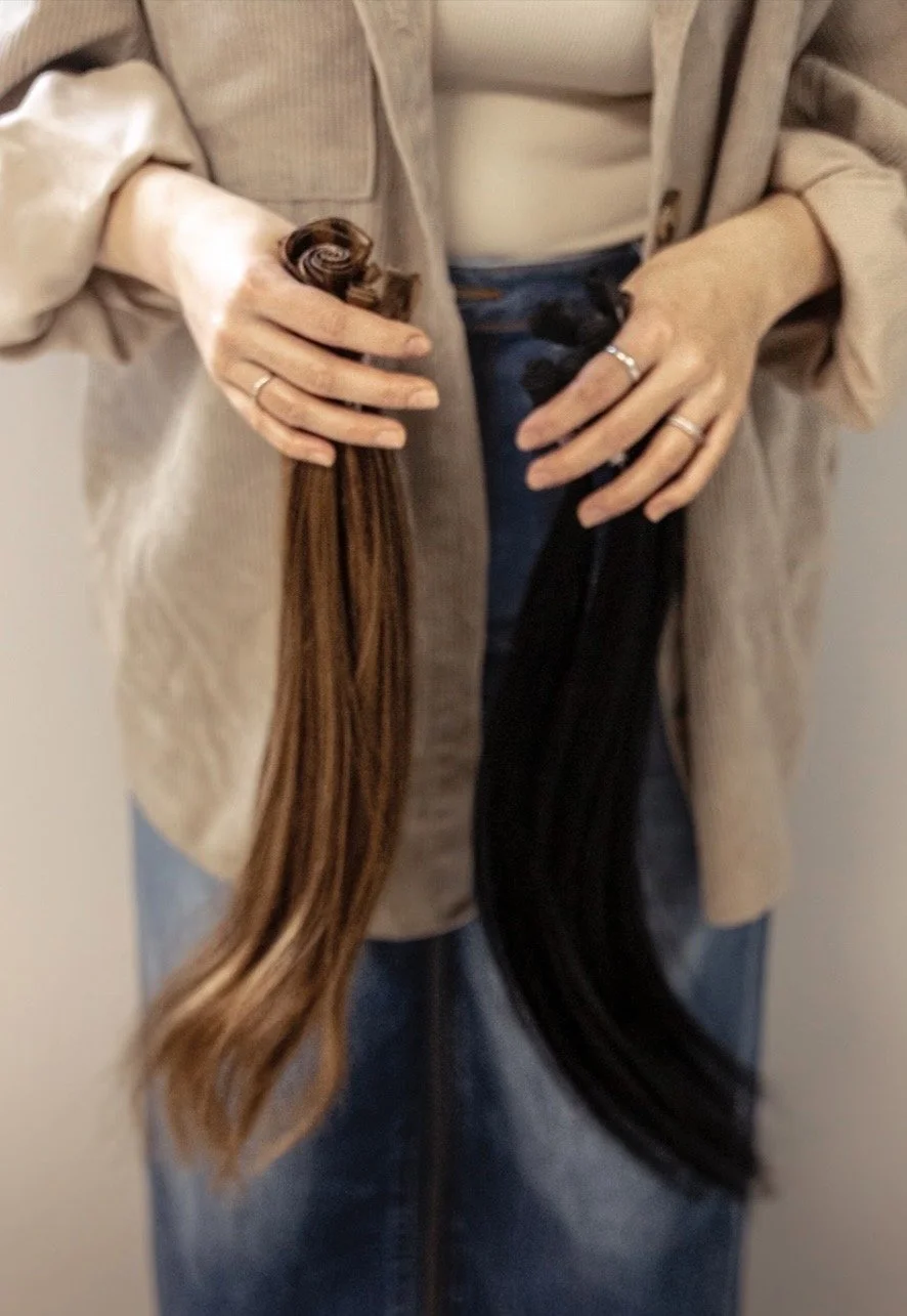 Person holding two hair extensions, one brown and one black, with both hands.