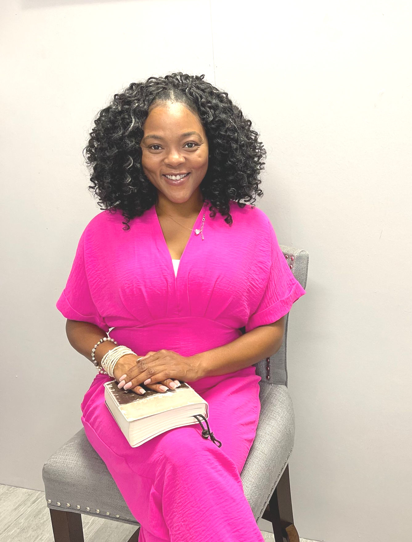 Sheenayvonne sitting in a chair with bible on her lap, while she is smiling at the camera