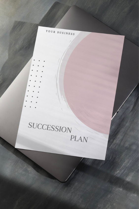 A mac laptop on top of a grayish black table with a mock succession plan guide.