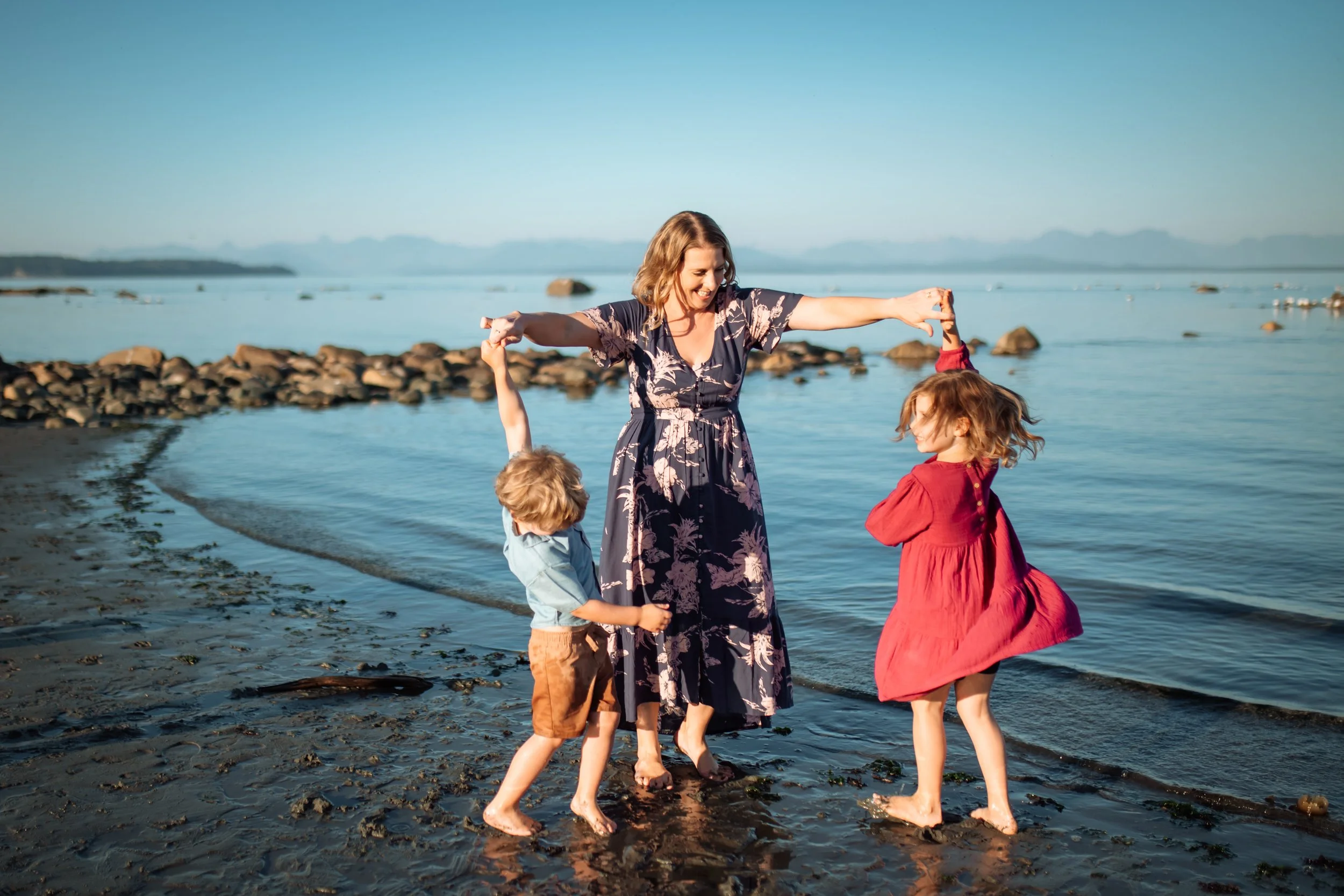 Alyson holding hands and dancing with her two kids in shallow water at the beach