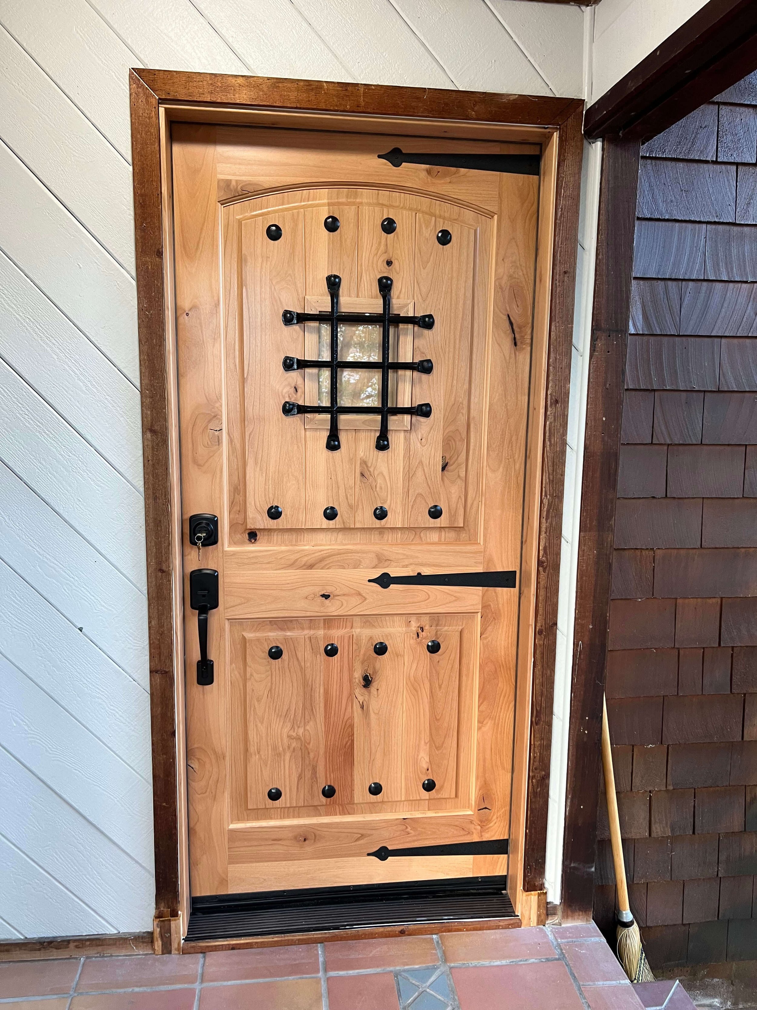 Custom solid wood front entry door with decorative iron grille, speakeasy window, and black hardware installed in Stockton, California.