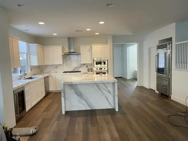 Modern kitchen remodeling project featuring custom white cabinets, quartz waterfall island, backsplash, and wood flooring installed by All About Carpentry Inc. in Stockton, California.
