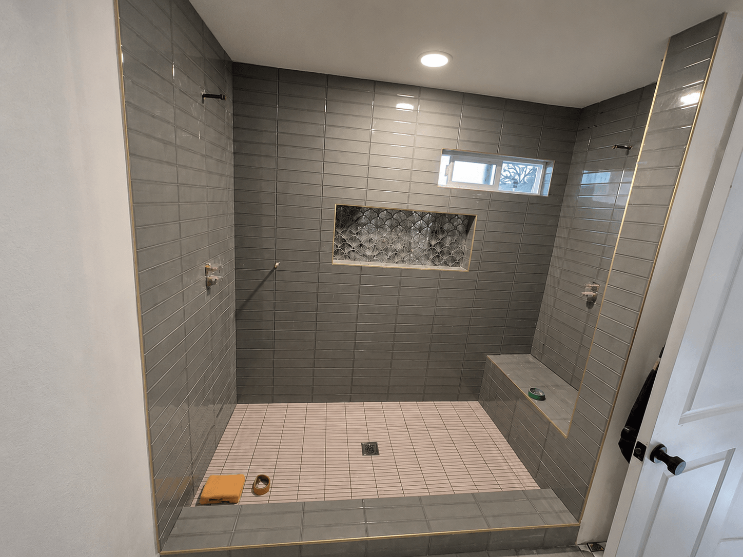 Custom walk-in shower remodel with gray subway tile, built-in bench, decorative shower niche, and frameless glass enclosure by All About Carpentry Inc. in Stockton, California.
