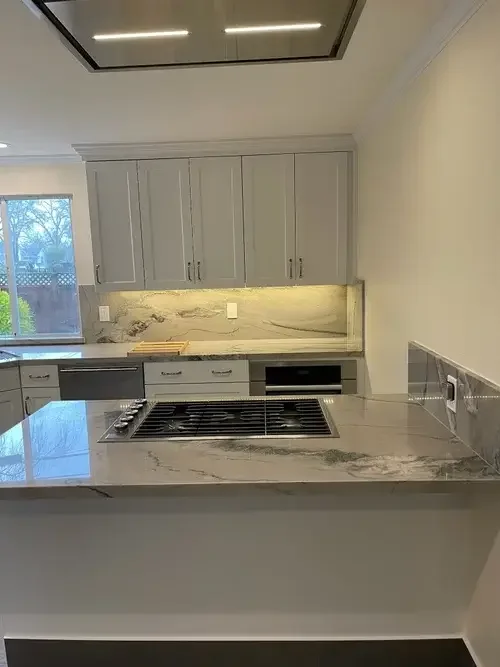 Custom kitchen remodel featuring white shaker cabinets, quartz countertops, full-height backsplash, and modern kitchen island installed by All About Carpentry Inc. in Stockton, California.