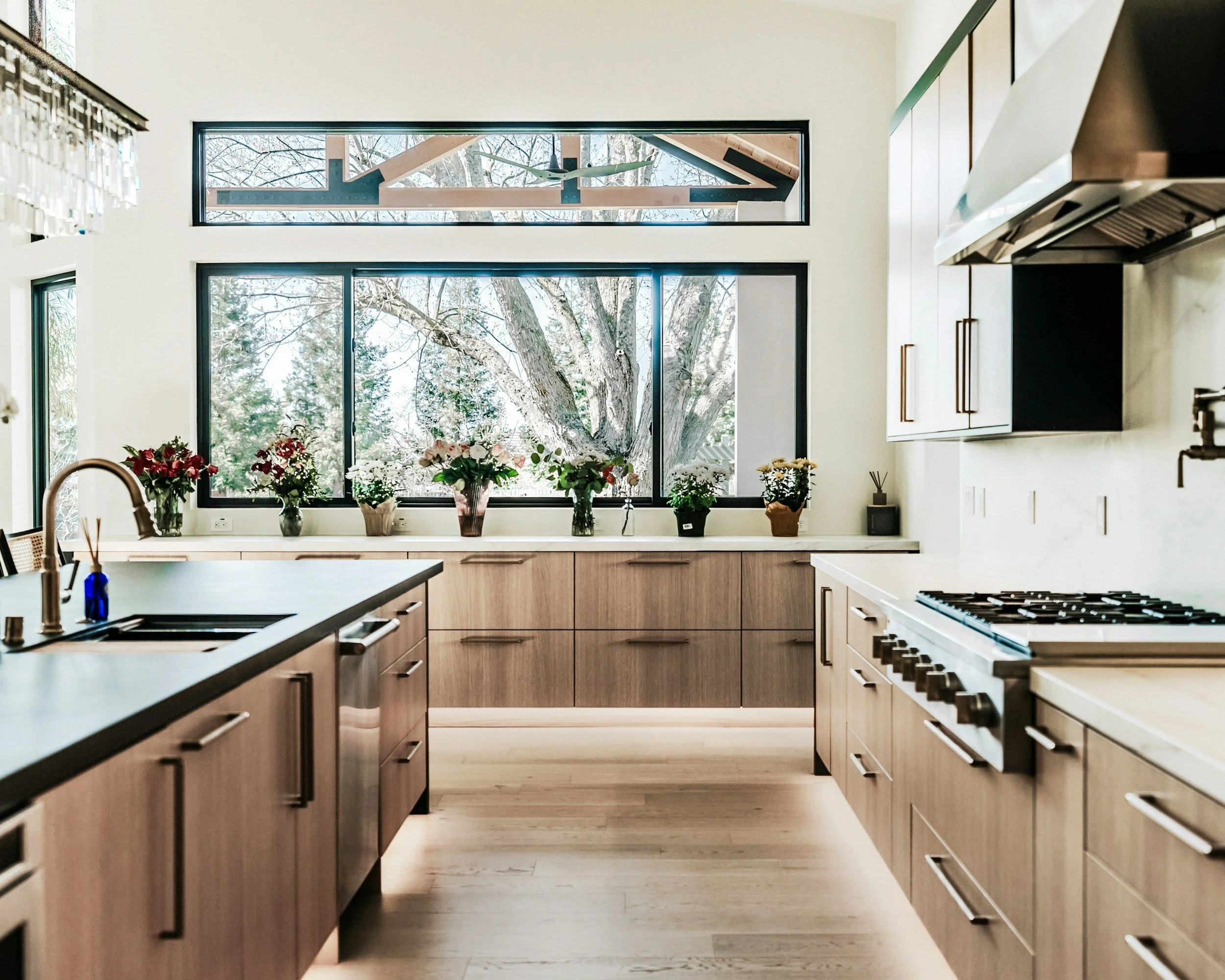 Modern kitchen with wood cabinets, large window with a view of a tree, and flowers on the countertop.