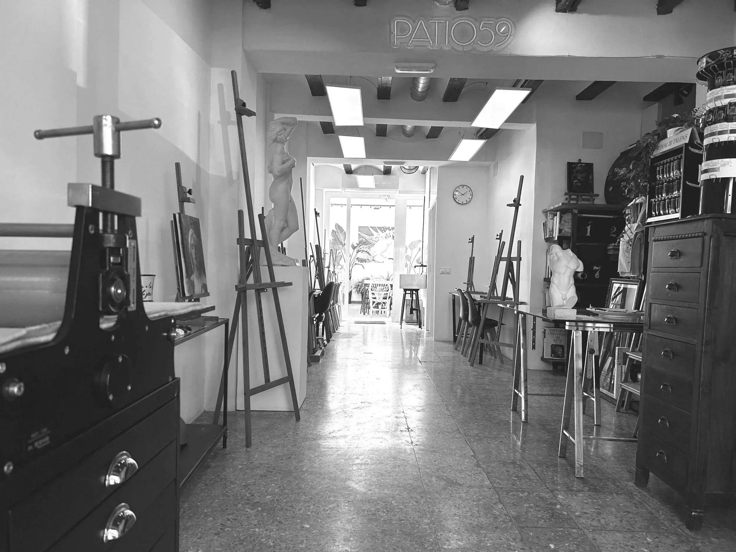 Interior de un estudio de arte con caballetes, esculturas, estanterías con libros y plantas, y diversos objetos decorativos.