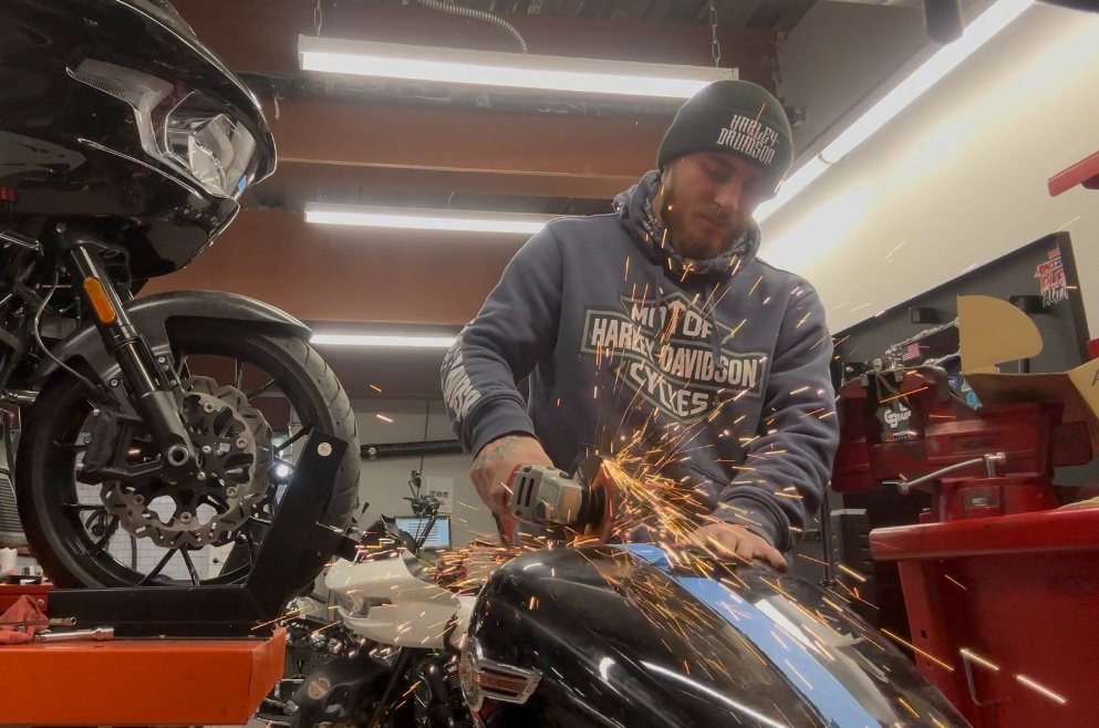 A man working on a motorcycle in a workshop, using a power tool that produces sparks.