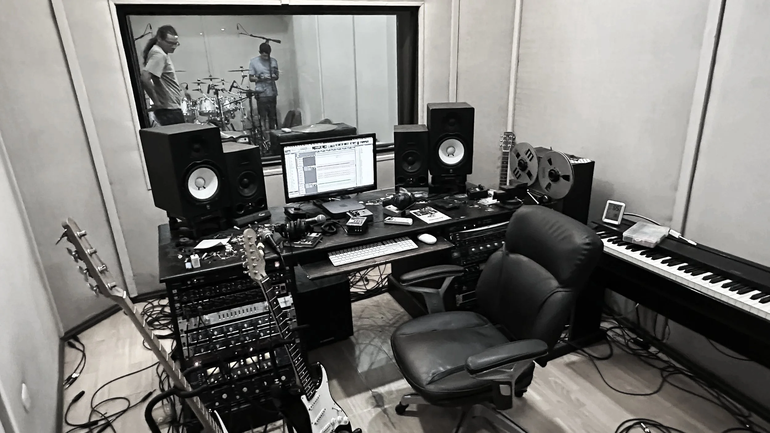 Music recording studio with mixing console, studio monitors, electric guitars, keyboard, computer, and recording equipment in a professional setup.