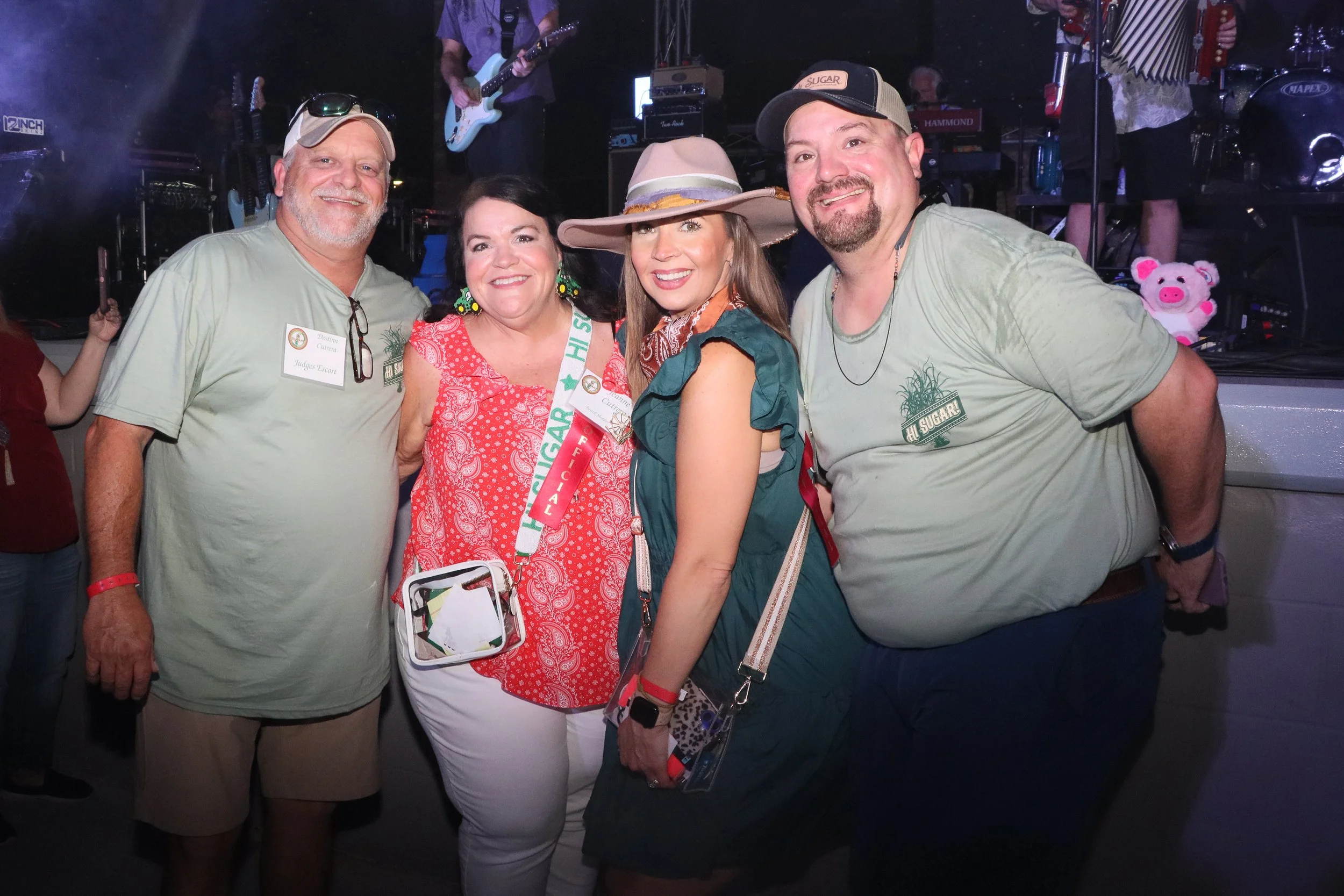 Group of four people smiling at the Louisiana Sugar Cane Festival Fais Do-Do with stage and musicians in the background.