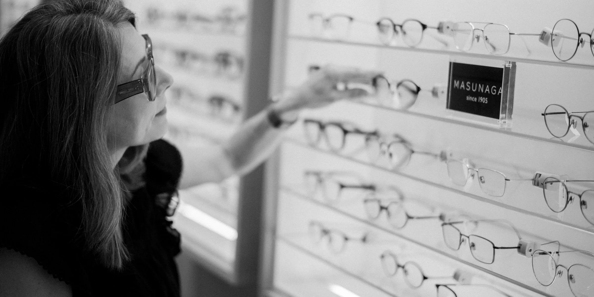 En svartvit stämningsfull bild av en optikerassistent i butiken hos Branning som noggrant sorterar glasögon på en hylla.
