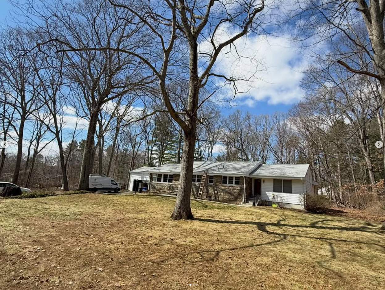A house on a lawn surrounded by leafless trees under a partly cloudy sky.