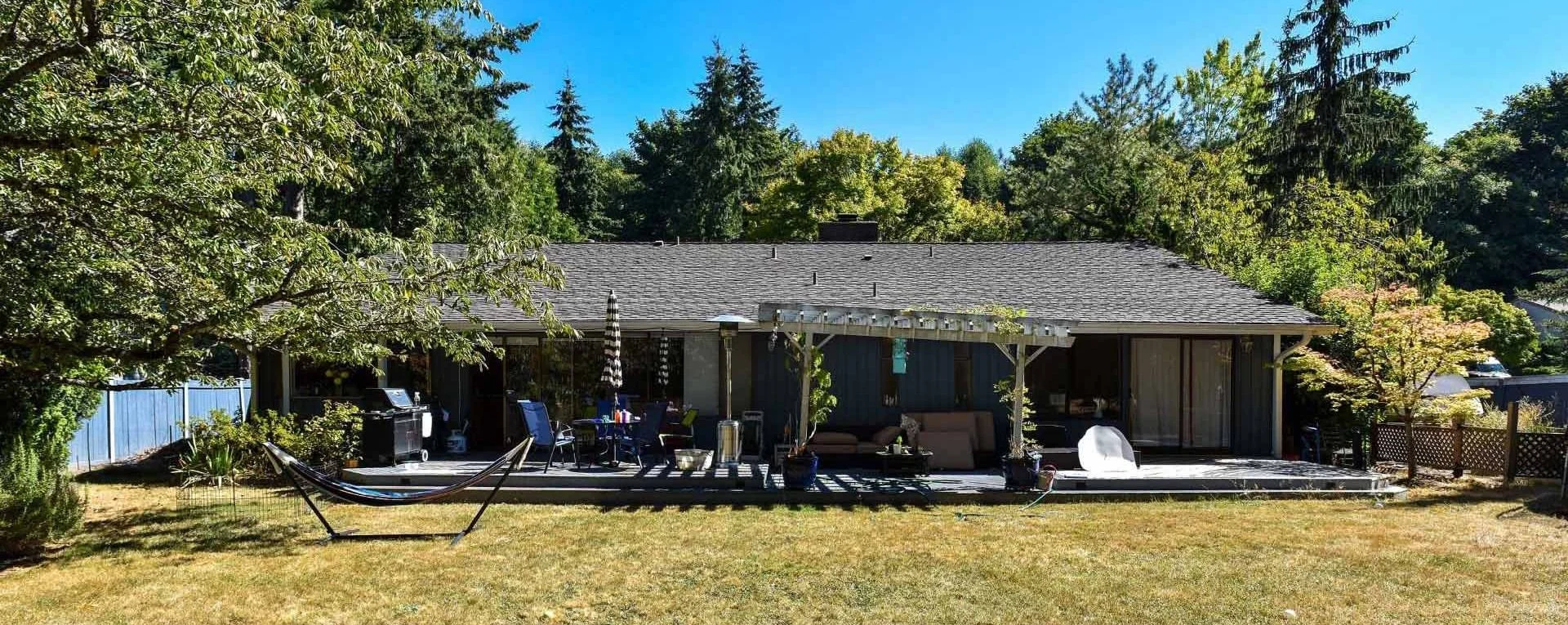 Backyard with a deck, outdoor furniture, hammock, barbecue grill, and surrounding trees