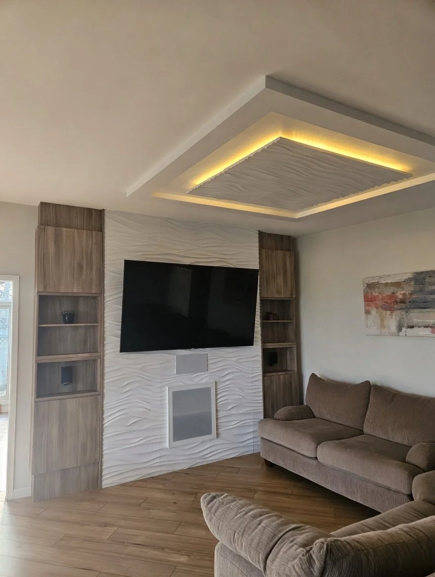 Living room with a mounted flat-screen TV on textured white wall, beige couch, wooden cabinetry, and abstract art on the wall.