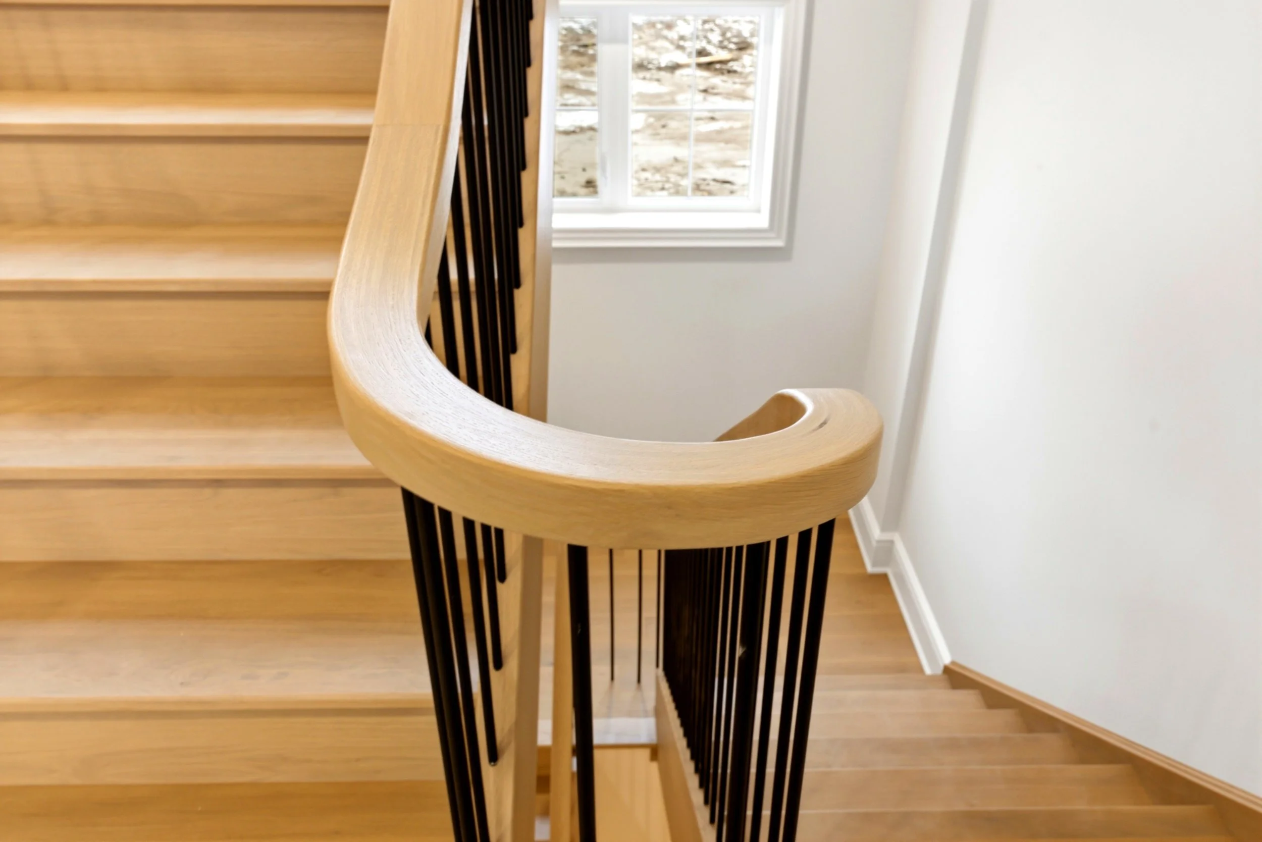 Wooden staircase with black metal railing, white walls, and a window showing an outdoor scene.