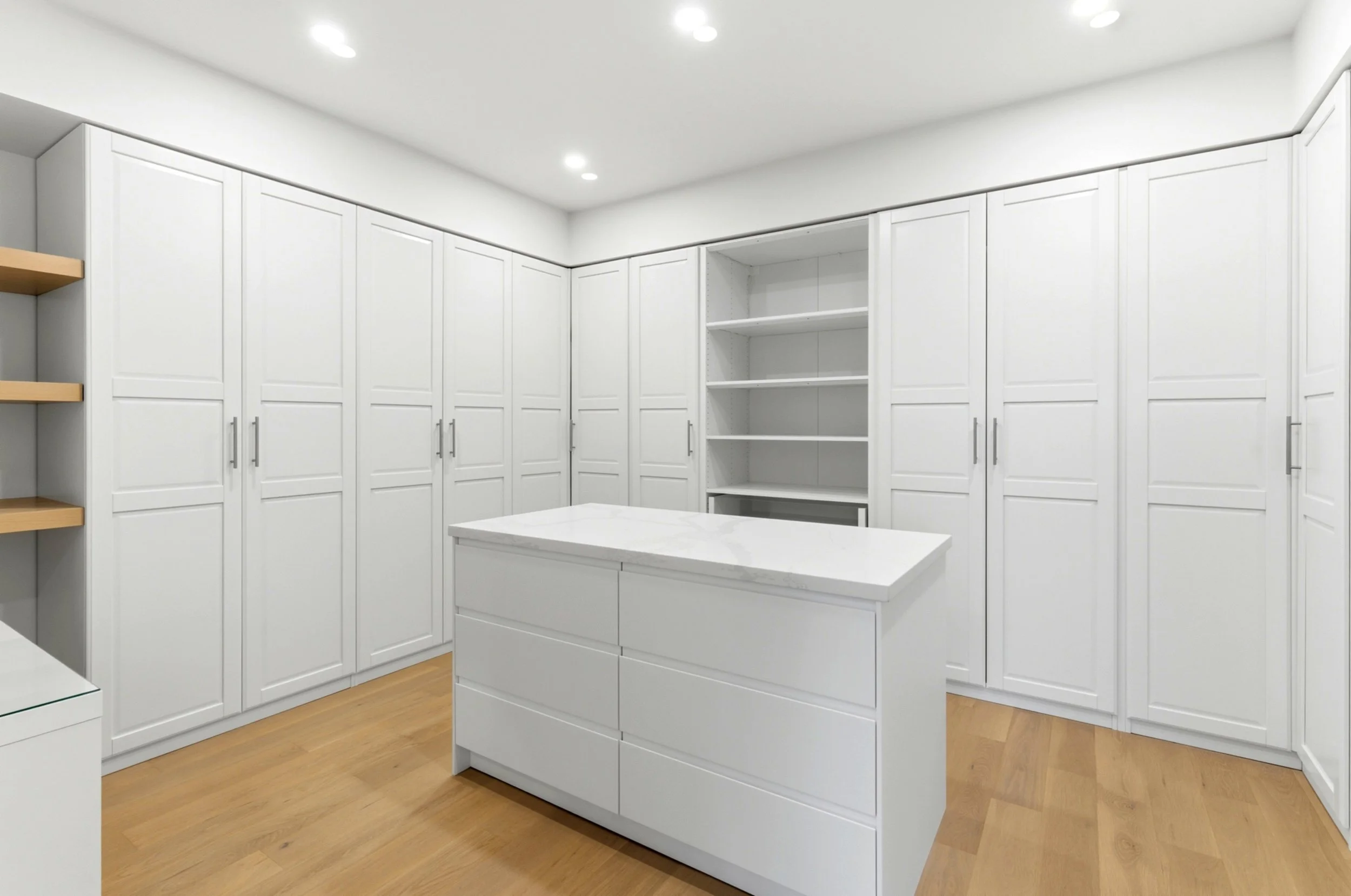 Empty walk-in closet with white cabinetry, open shelves, a small island with drawers, and wooden flooring.