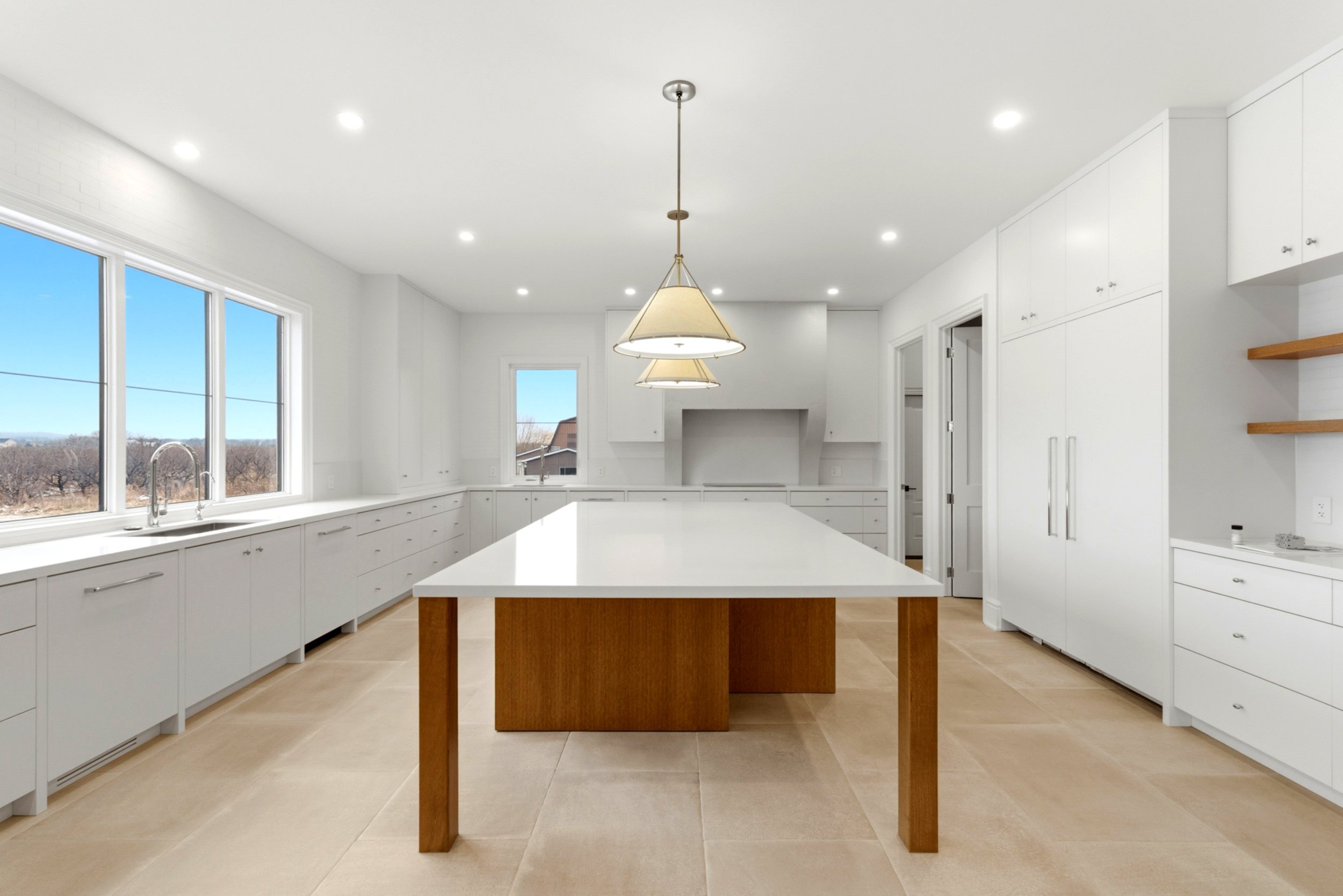 Bright, spacious kitchen with white cabinets, large island with a white countertop and wooden base, multiple windows, and modern appliances.