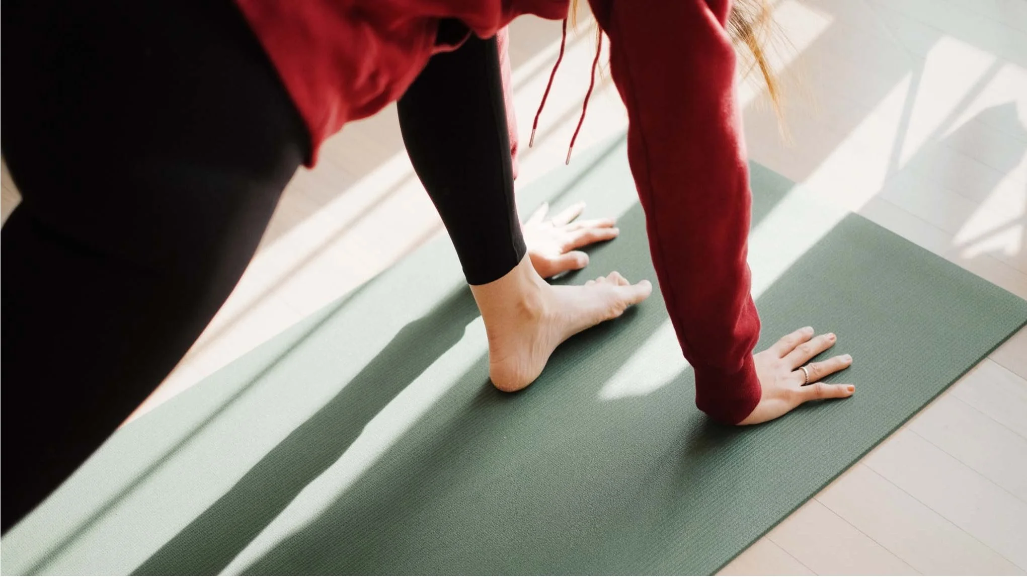 Close-up of a woman performing yoga, in downward dog pose on a green mat.