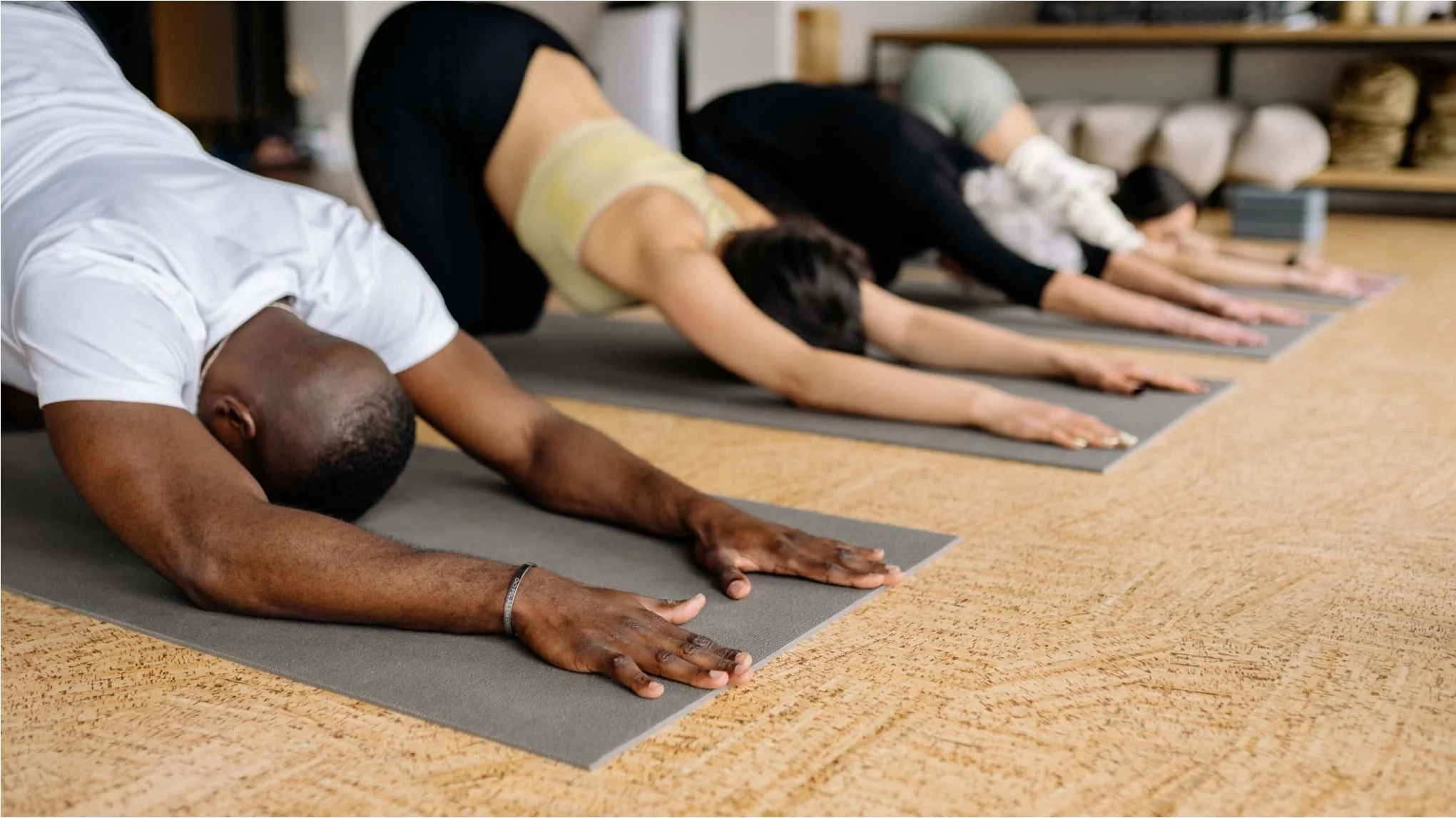 People participating in a yoga class, doing forward bends on yoga mats.