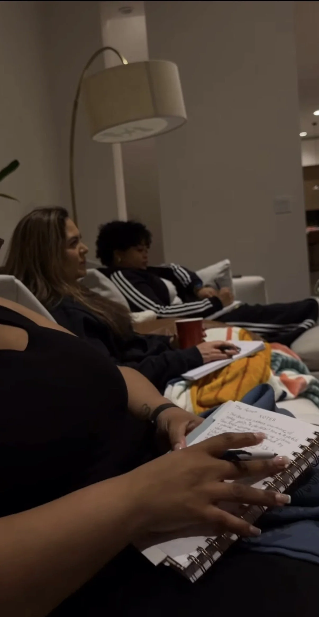 People sitting on a couch, some taking notes, in a dimly lit room.
