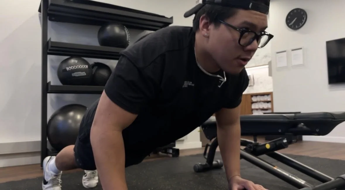 Person performing a push-up exercise on a gym floor with fitness equipment in the background.