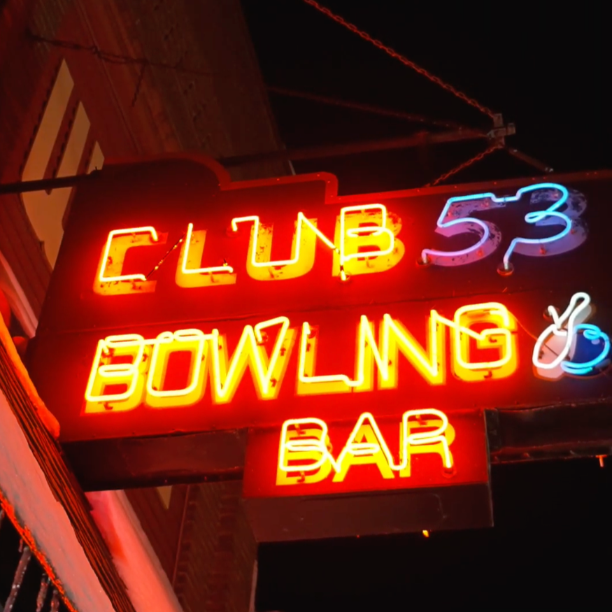 Neon sign reading 'Club 53 Bowling Bar' with a bowling ball and pin icon, illuminated at night.