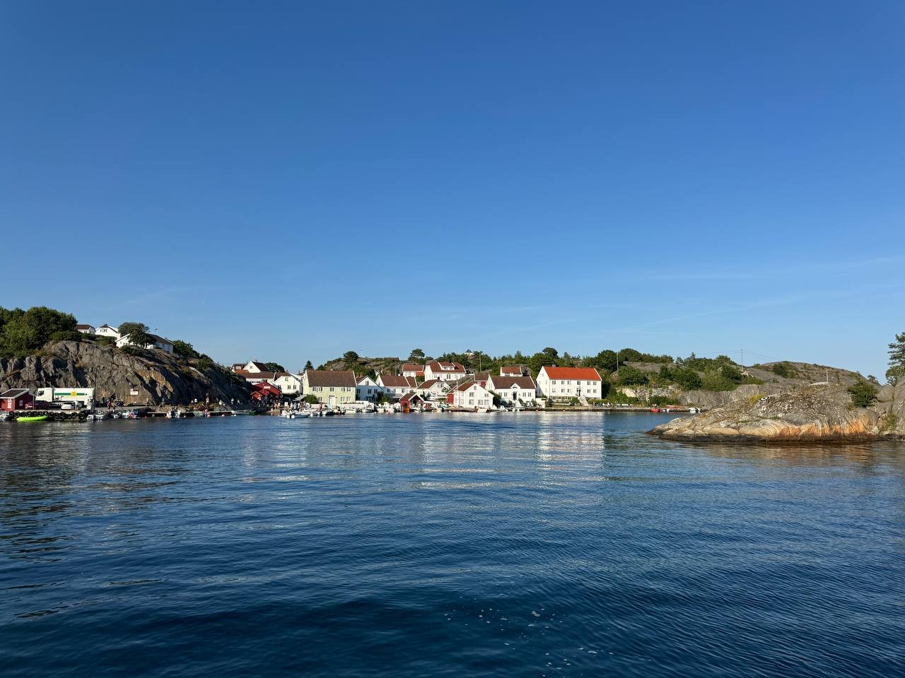 A peaceful coastal village with colorful houses along the shoreline and calm water in the foreground, under a clear blue sky.