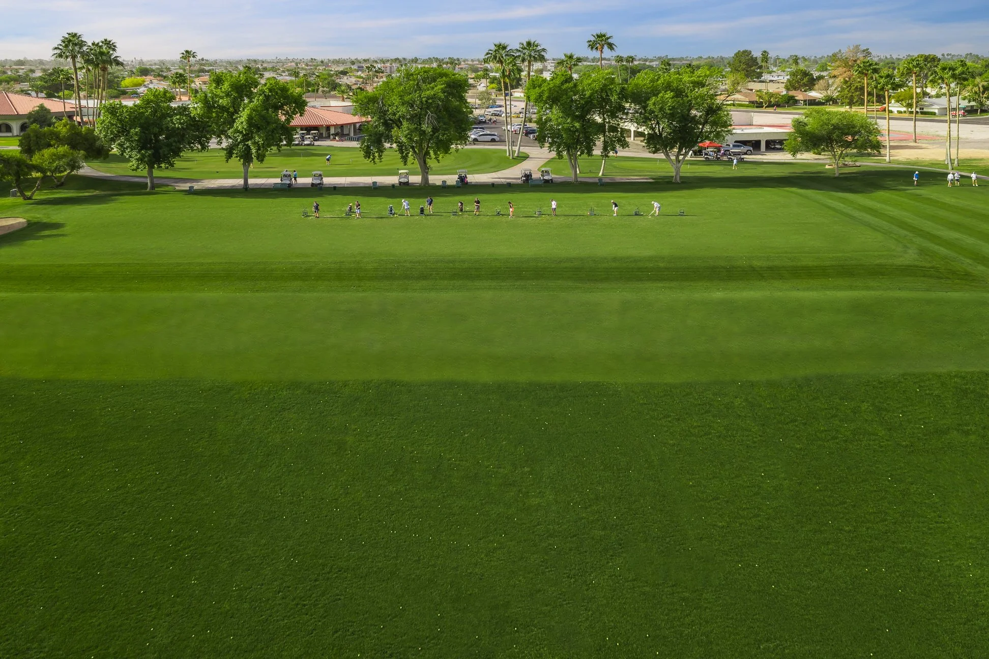 A golf course with green fairways, trees, and people walking with golf carts in the background.