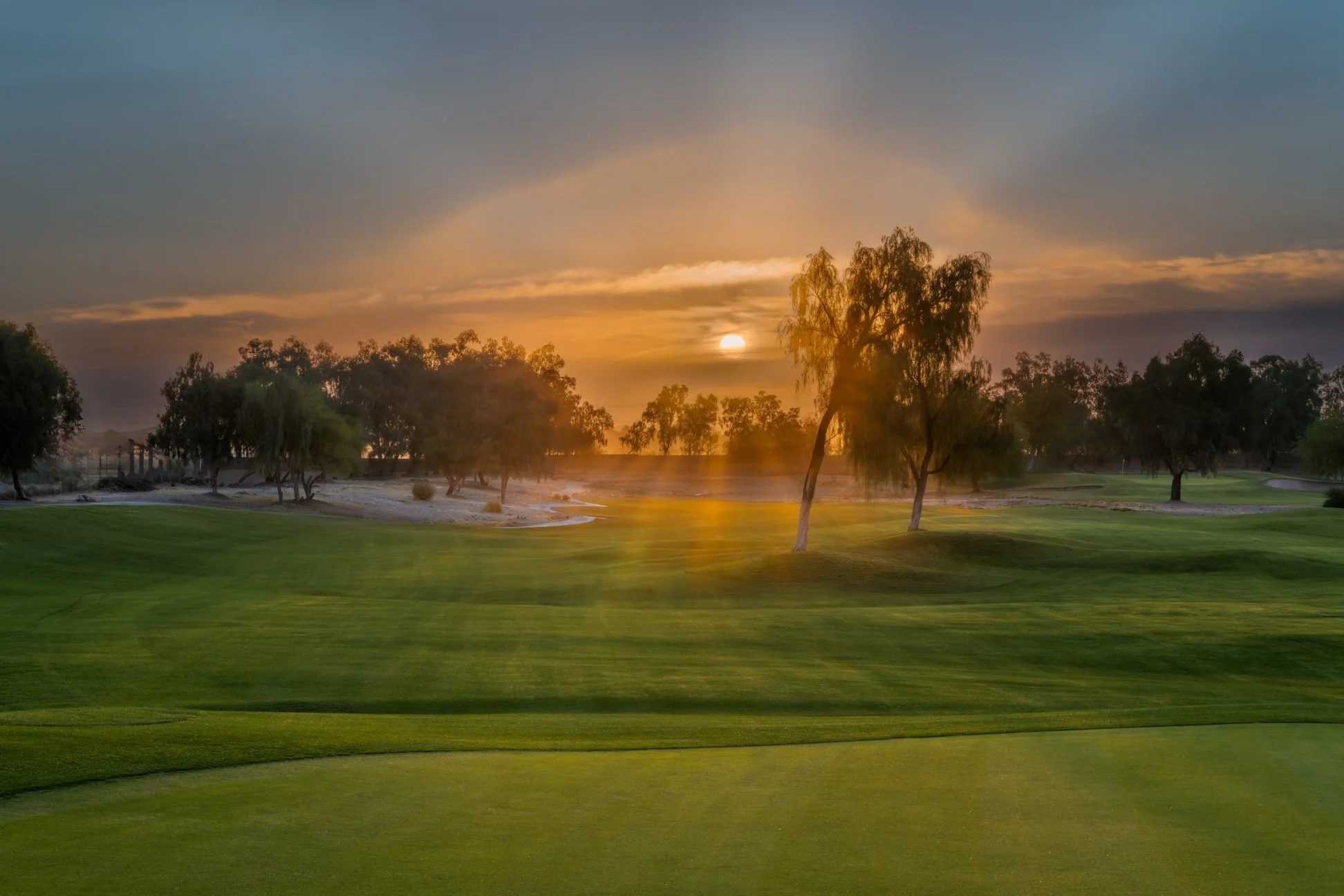 Sunrise over Coyote Lakes Golf Club in Surprise, Arizona with green grass, trees, and a partly cloudy sky.