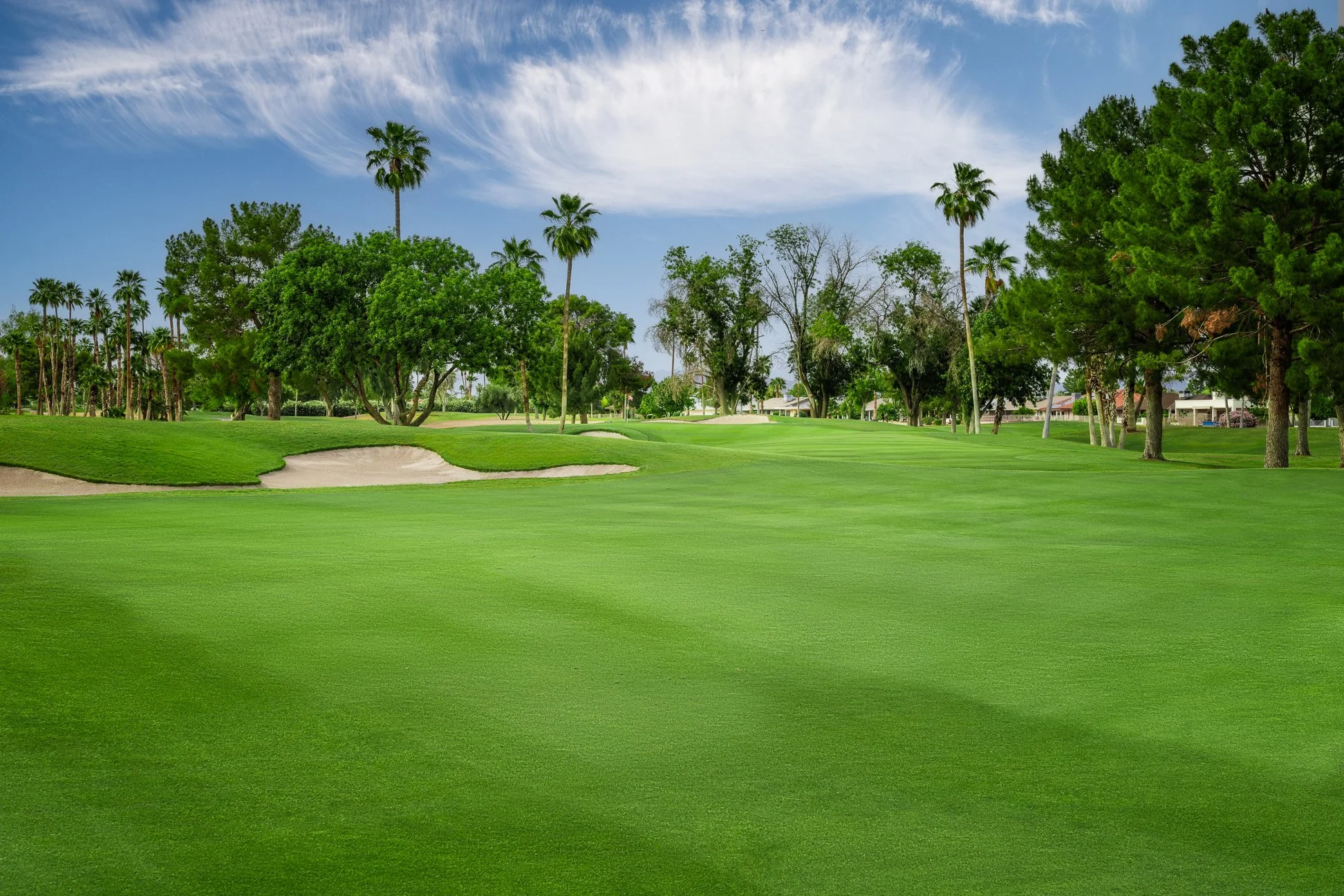 A lush green golf course with sand traps, trees, and a partly cloudy sky on the 15th hole at Briarwood Country Club in Sun City West Arizona.