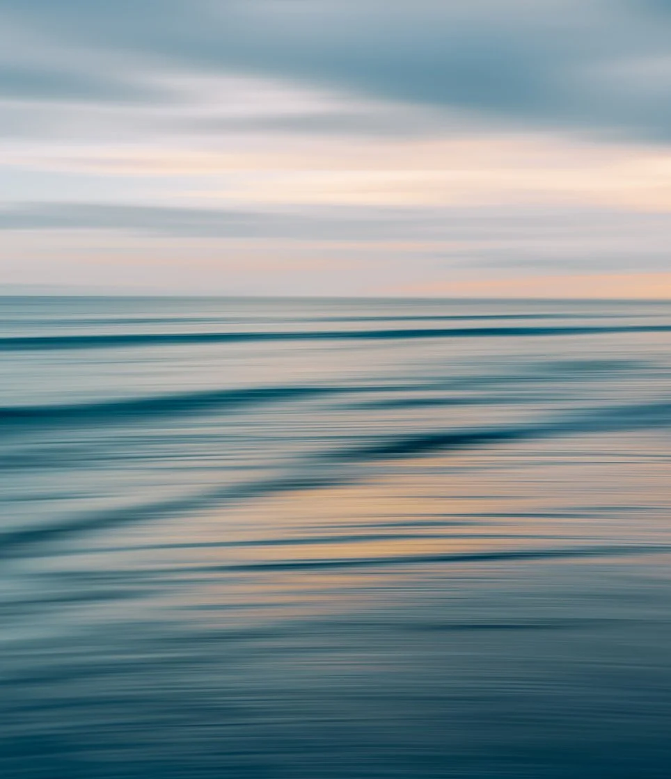 Une mer calme avec des vagues mouettes et un ciel nuageux au coucher ou lever du soleil avec des couleurs pastel.