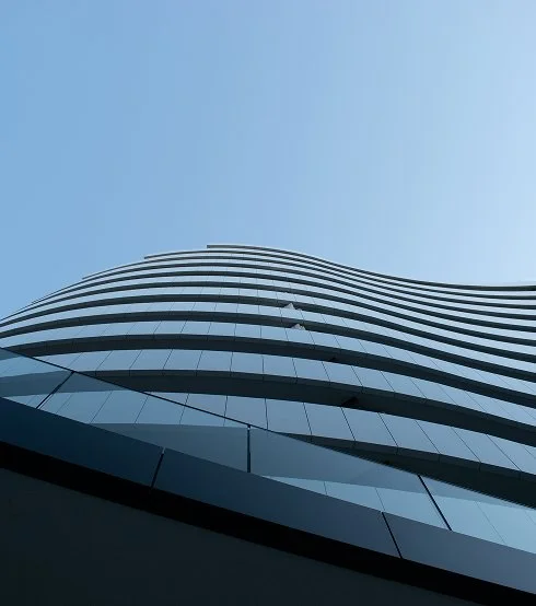 Vue en contre-plongée d'un gratte-ciel moderne avec des fenêtres en verre ondulées contre un ciel clair.
