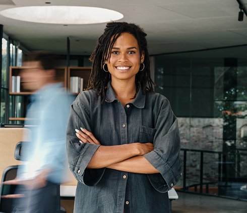 Jeune femme souriante avec dreadlocks et vêtements décontractés, dans un environnement moderne, probablement un bureau.