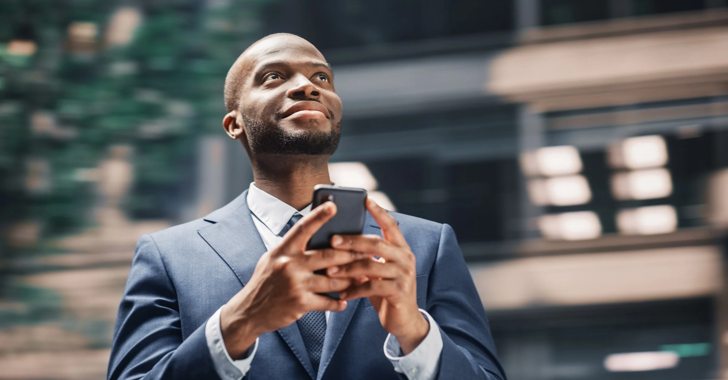 Homme d'affaires en costume cravate tient un smartphone dans un environnement urbain moderne.