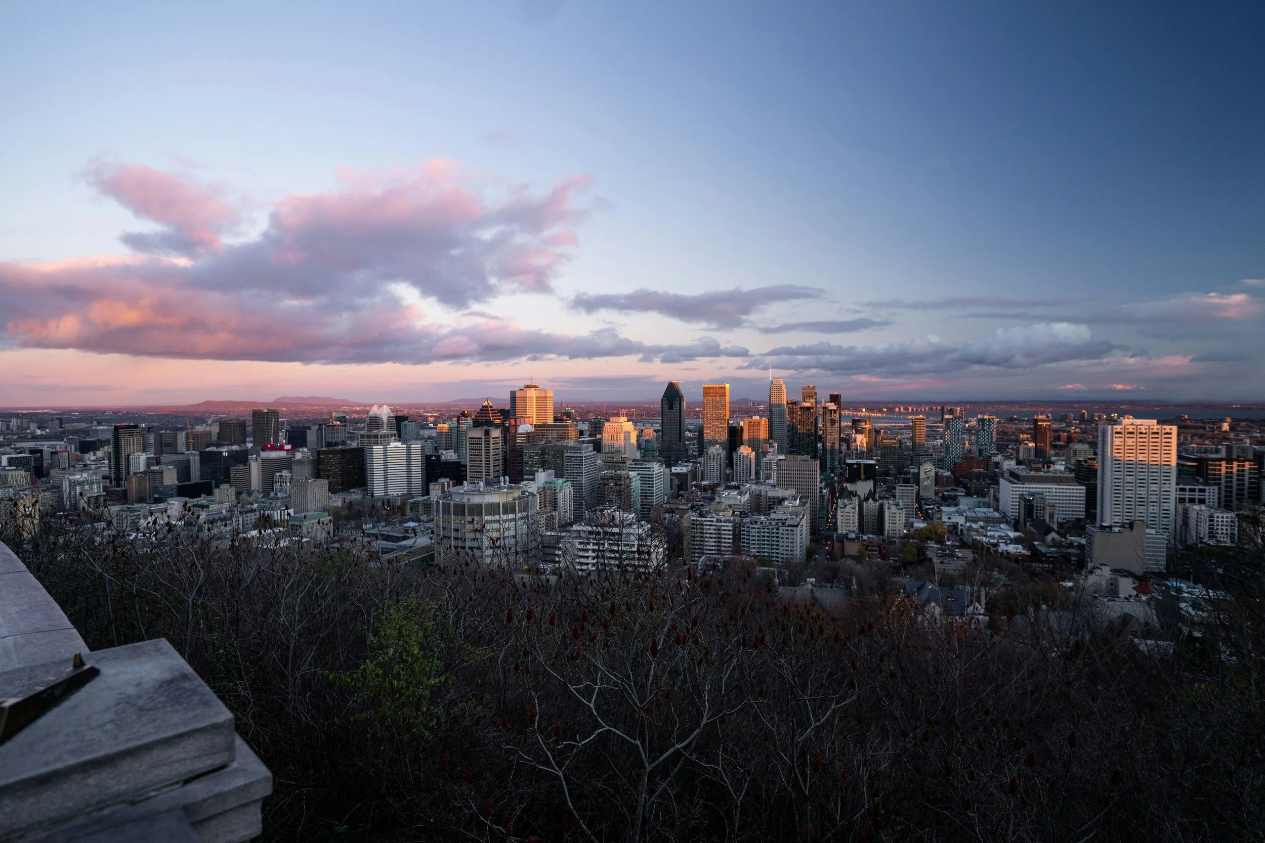 Une vue panoramique d'une ville avec de hauts bâtiments modernes au crépuscule, sous un ciel partiellement nuageux avec des teintes rose et bleu.