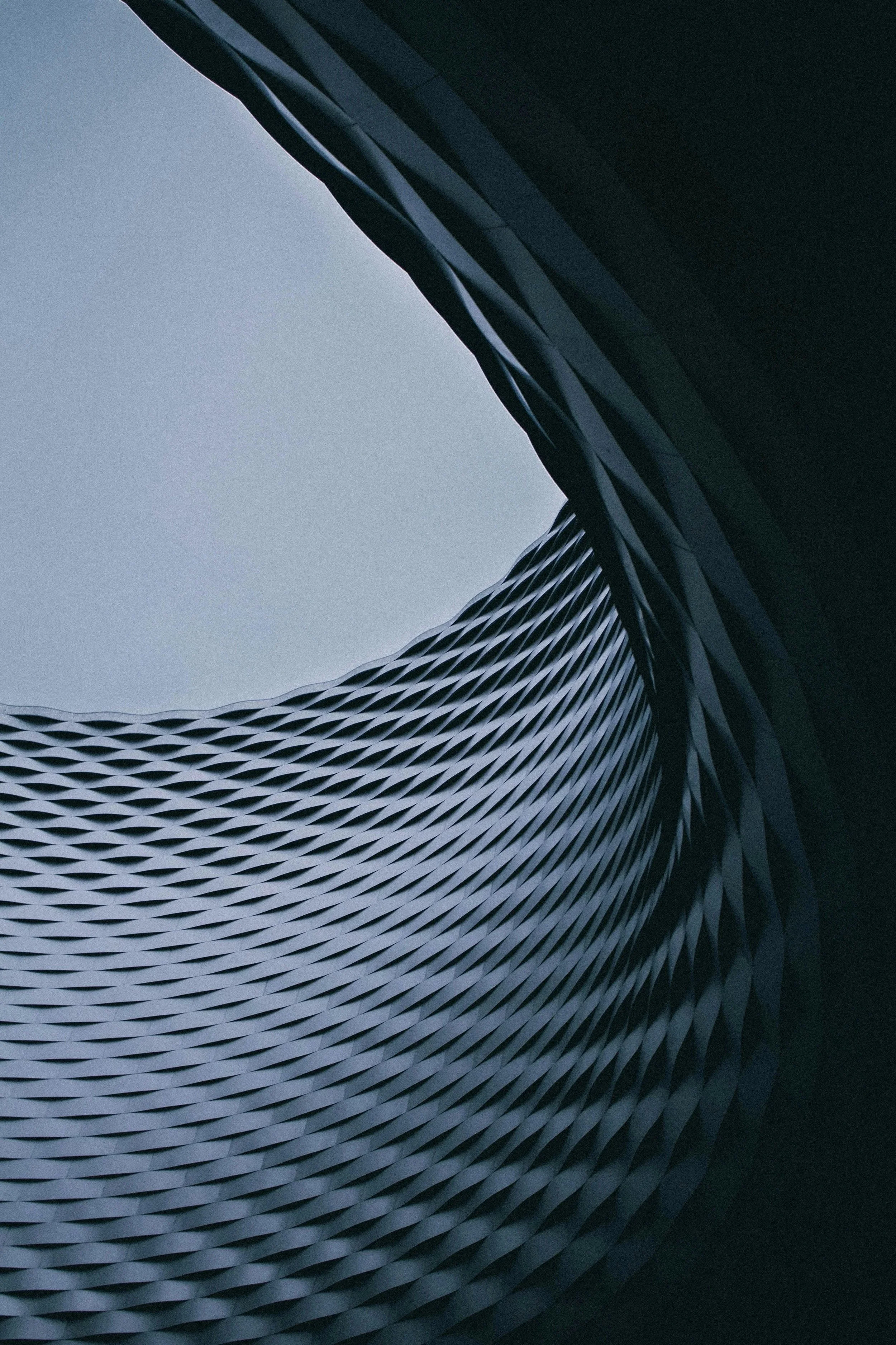 Une vue en plongée d'une architecture moderne avec des formes courbes et des motifs géométriques en métal, sous un ciel clair.