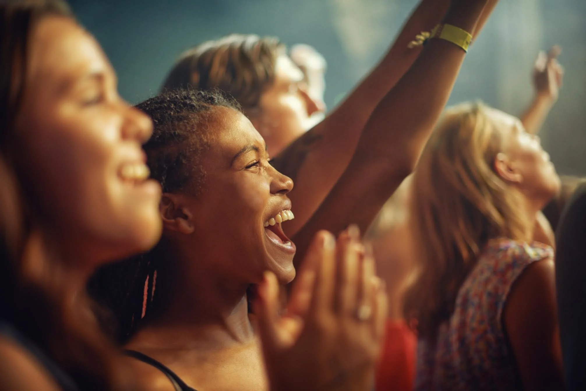 A group of diverse young women smiling and raising their arms in excitement at an event or concert.