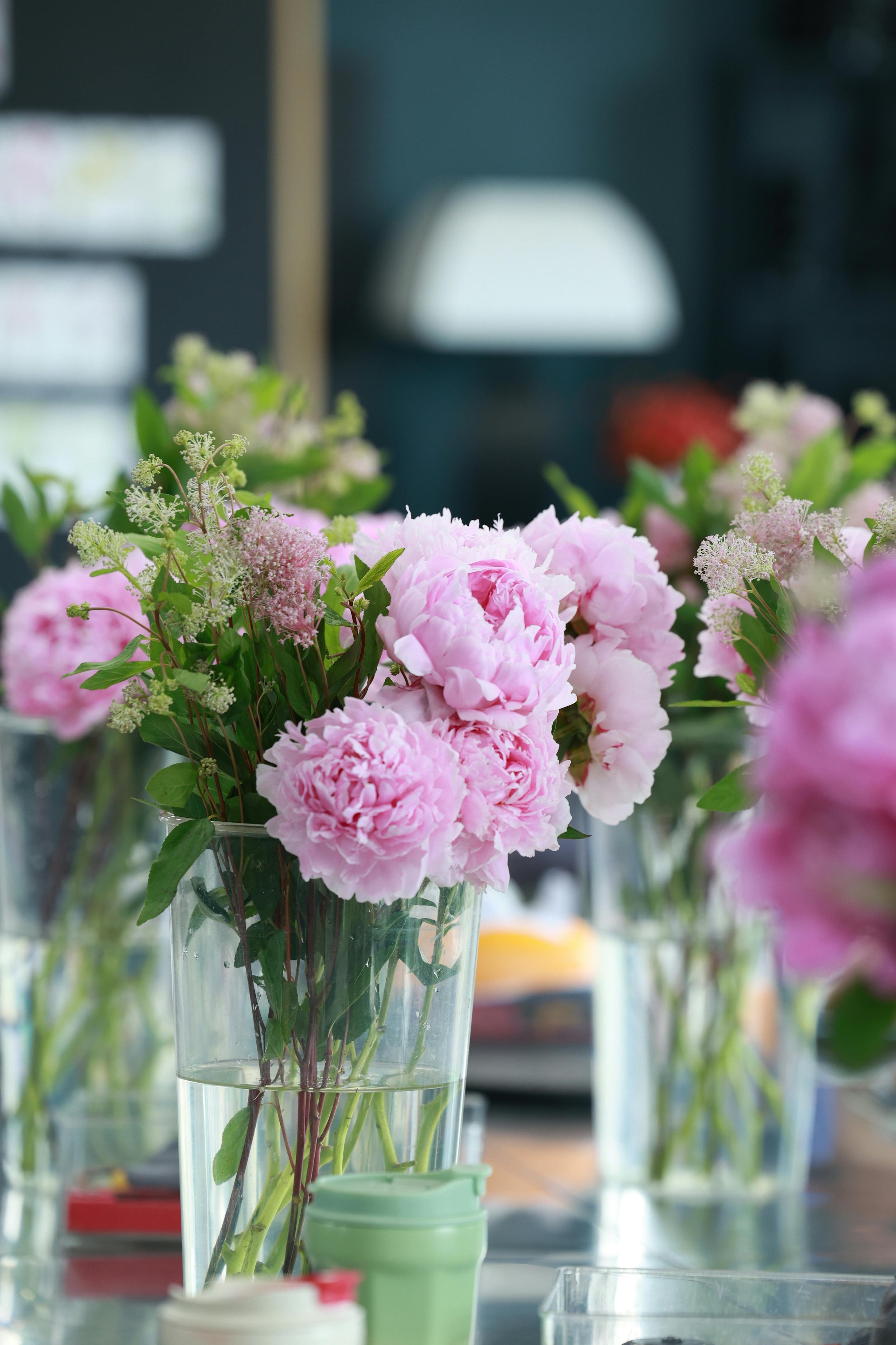 Close-up of pink and white flowers in glass vases, blurred background with laboratory or workspace setting.